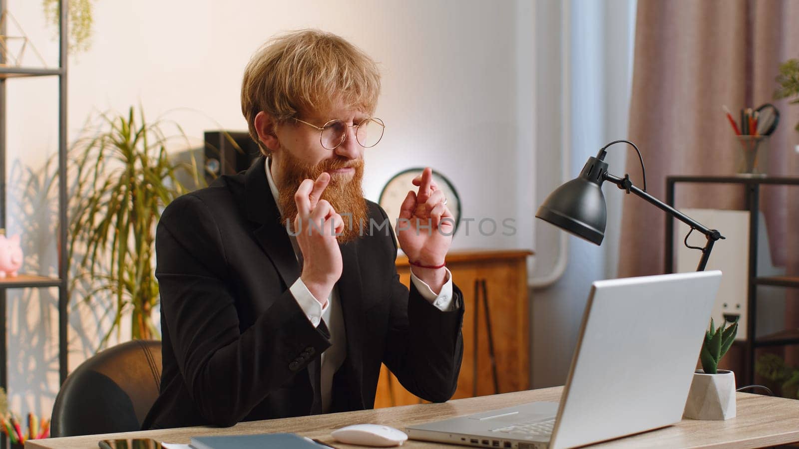 Young businessman working on laptop computer at home office desk crossed fingers looking at screen asking for good luck news, wishing good exam results, dreaming about win victory in lottery jackpot