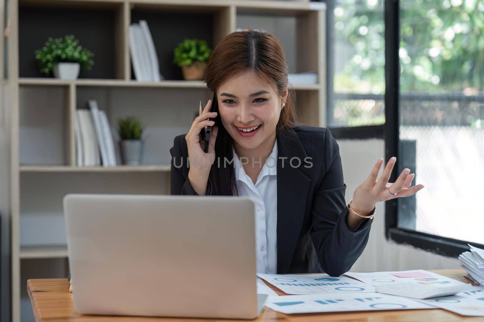 Happy young asian business woman talking on the mobile phone and smiling while sitting at her working place in office.