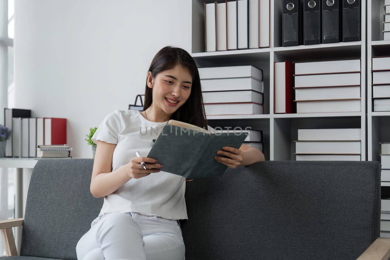 Happy young Asian businesswoman working and taking notes in home.