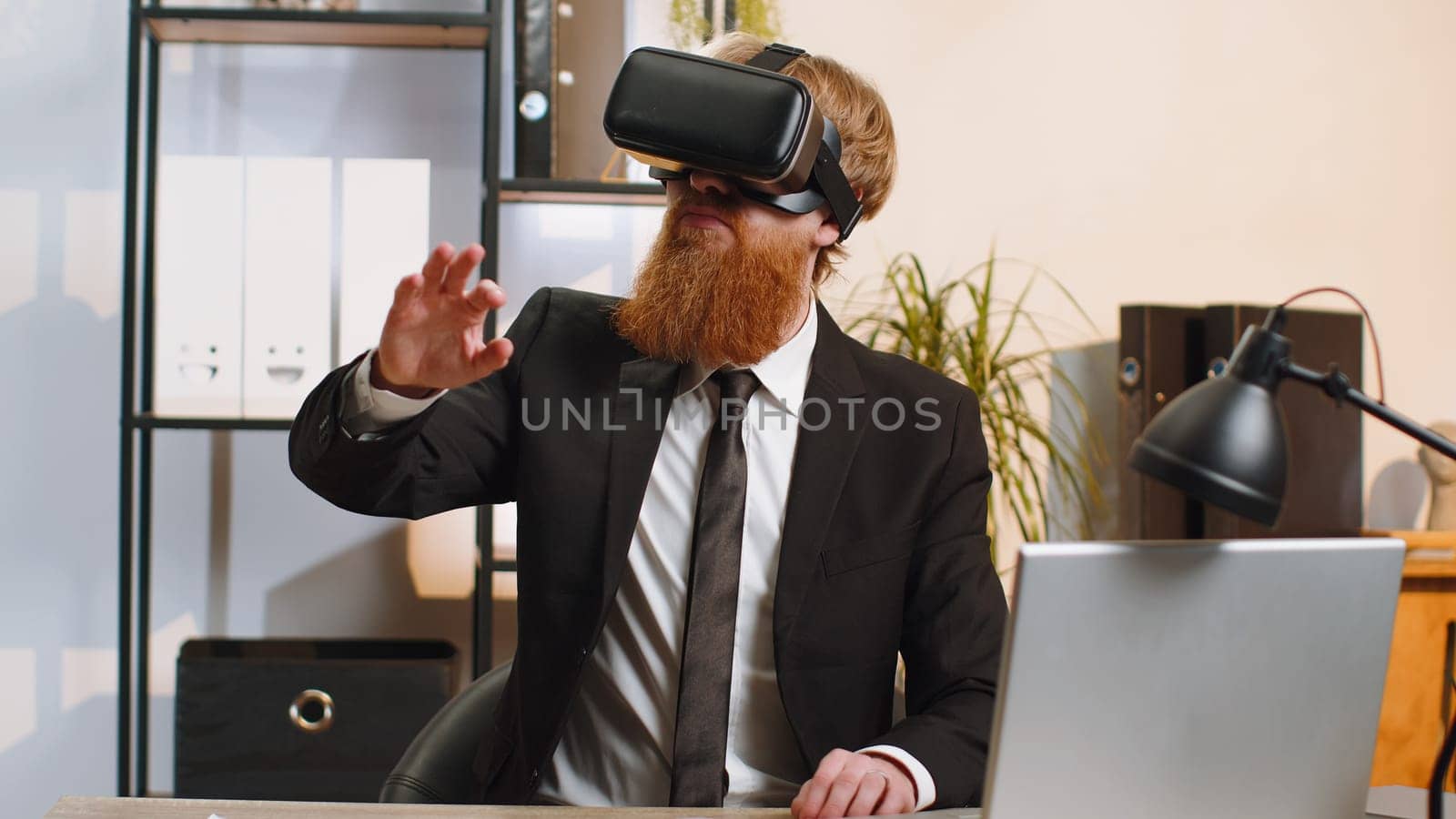 Young redhead businessman programmer software developer using headset helmet app to play simulation game. Watching virtual reality 3D 360 video. Young bearded in VR goggles working at home office