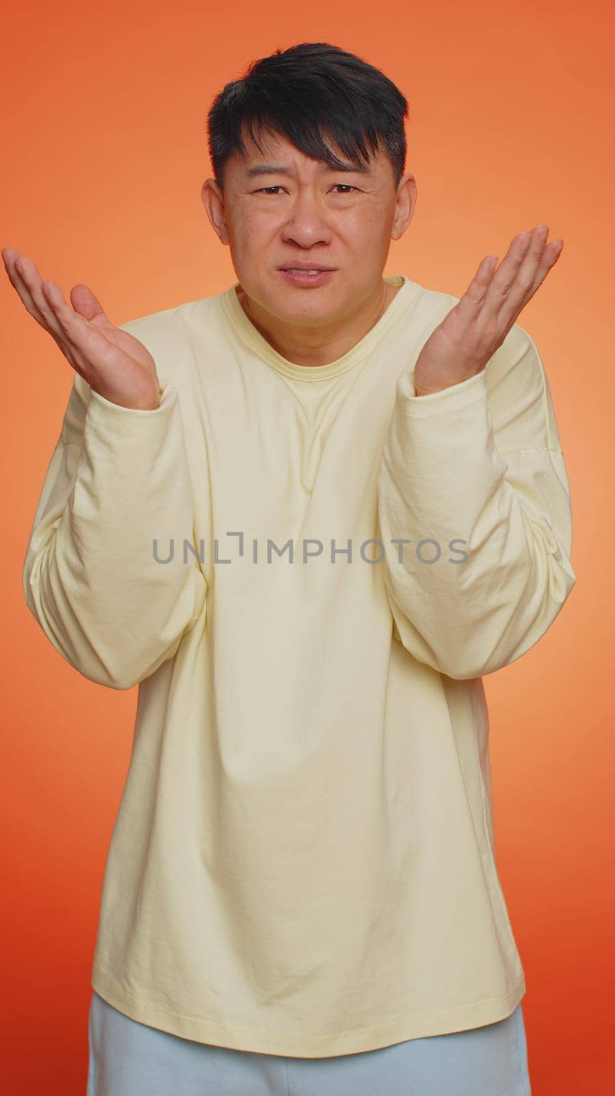 What Why. Sincere irritated asian man raising hands in indignant expression asking reason of failure demonstrating disbelief irritation by trouble. Confused guy on orange background. Vertical