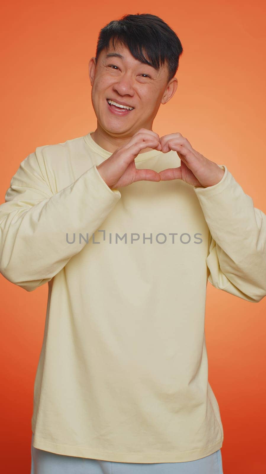 Smiling chinese man makes heart gesture demonstrates love sign expresses good feelings and sympathy by efuror