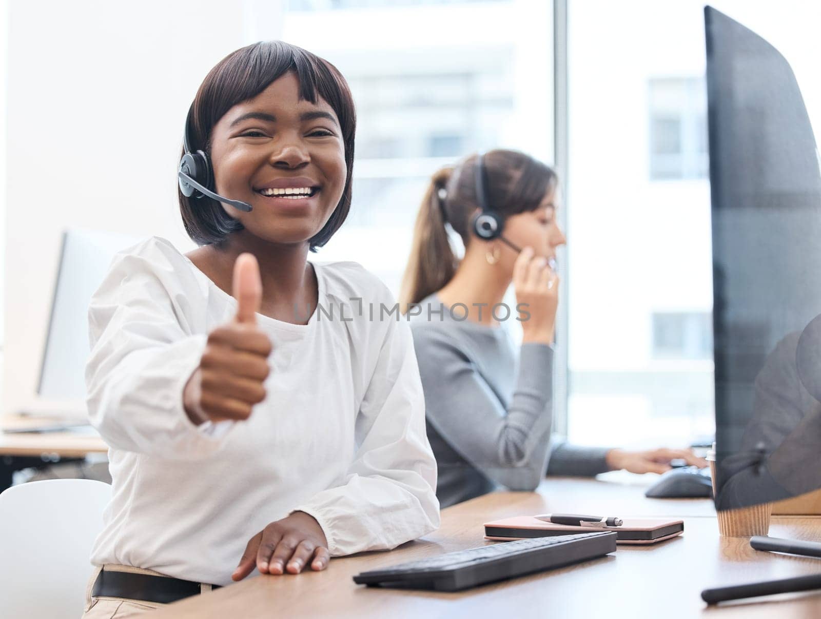 Thumbs up, woman with headset and on a computer desk in her office at work. Telemarketing or customer service, online communication or consultant and crm with African female person at workspace by YuriArcurs