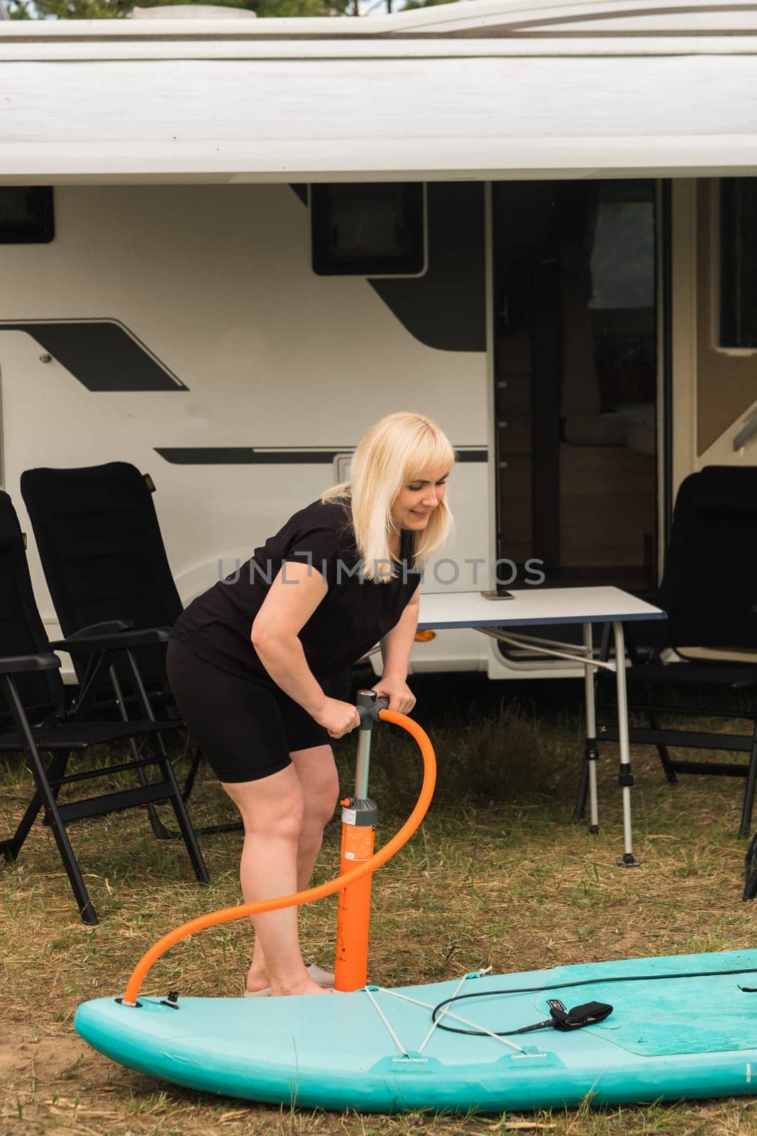 A woman inflates a sup-board for swimming near her motorhome.