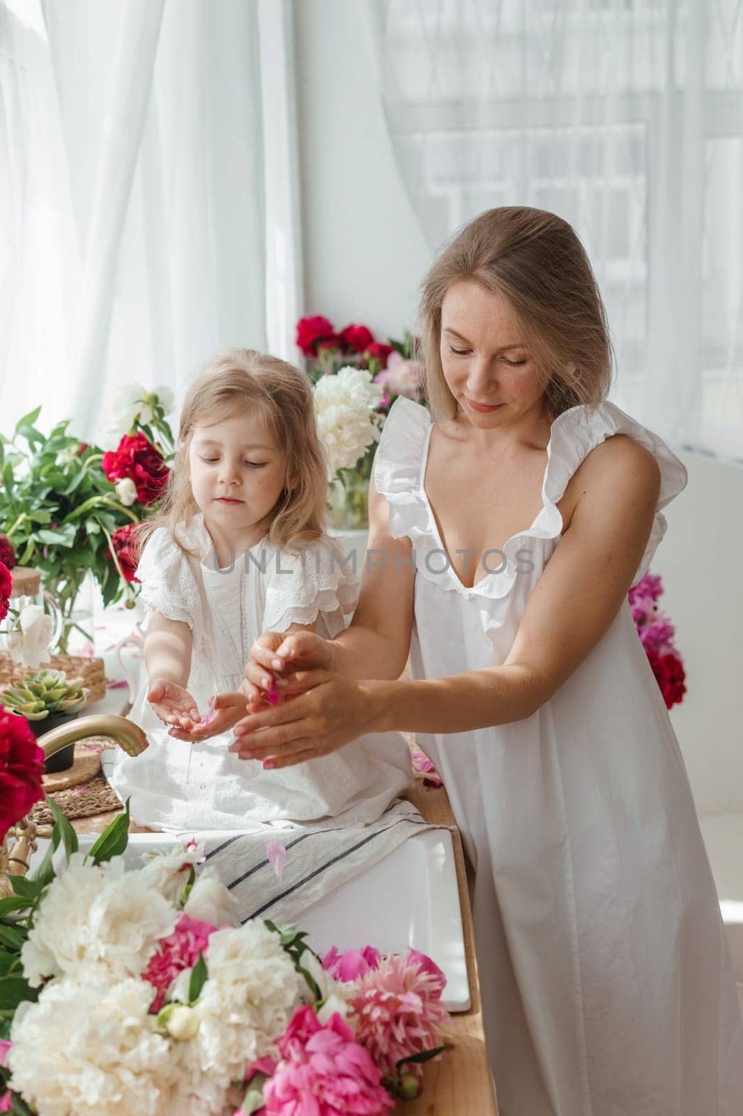 A little blonde girl with her mom on a kitchen countertop decorated with peonies. The concept of the relationship between mother and daughter. Spring atmosphere