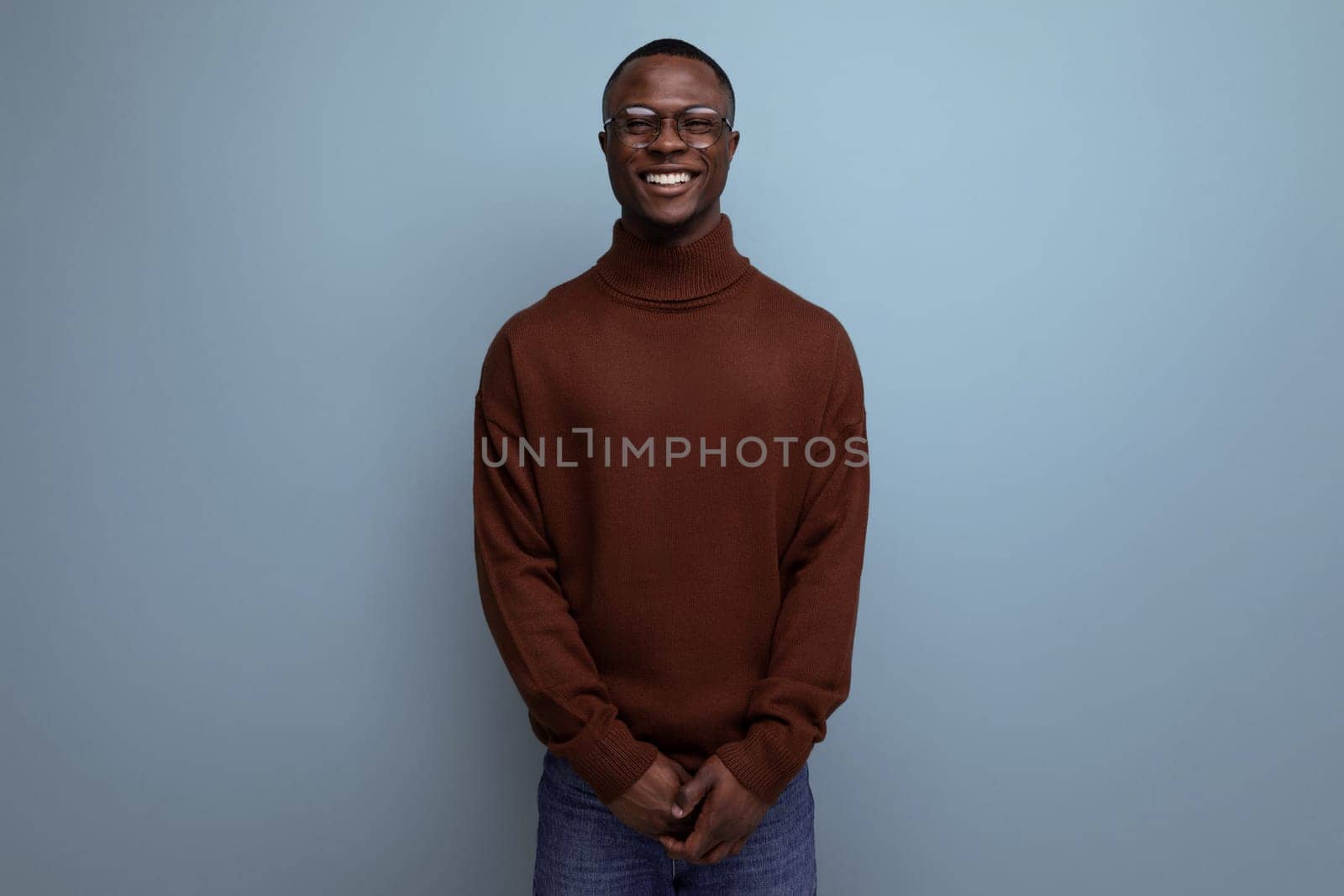 elegant young african brunet male businessman in stylish brown sweater and glasses on studio background with copy space by TRMK