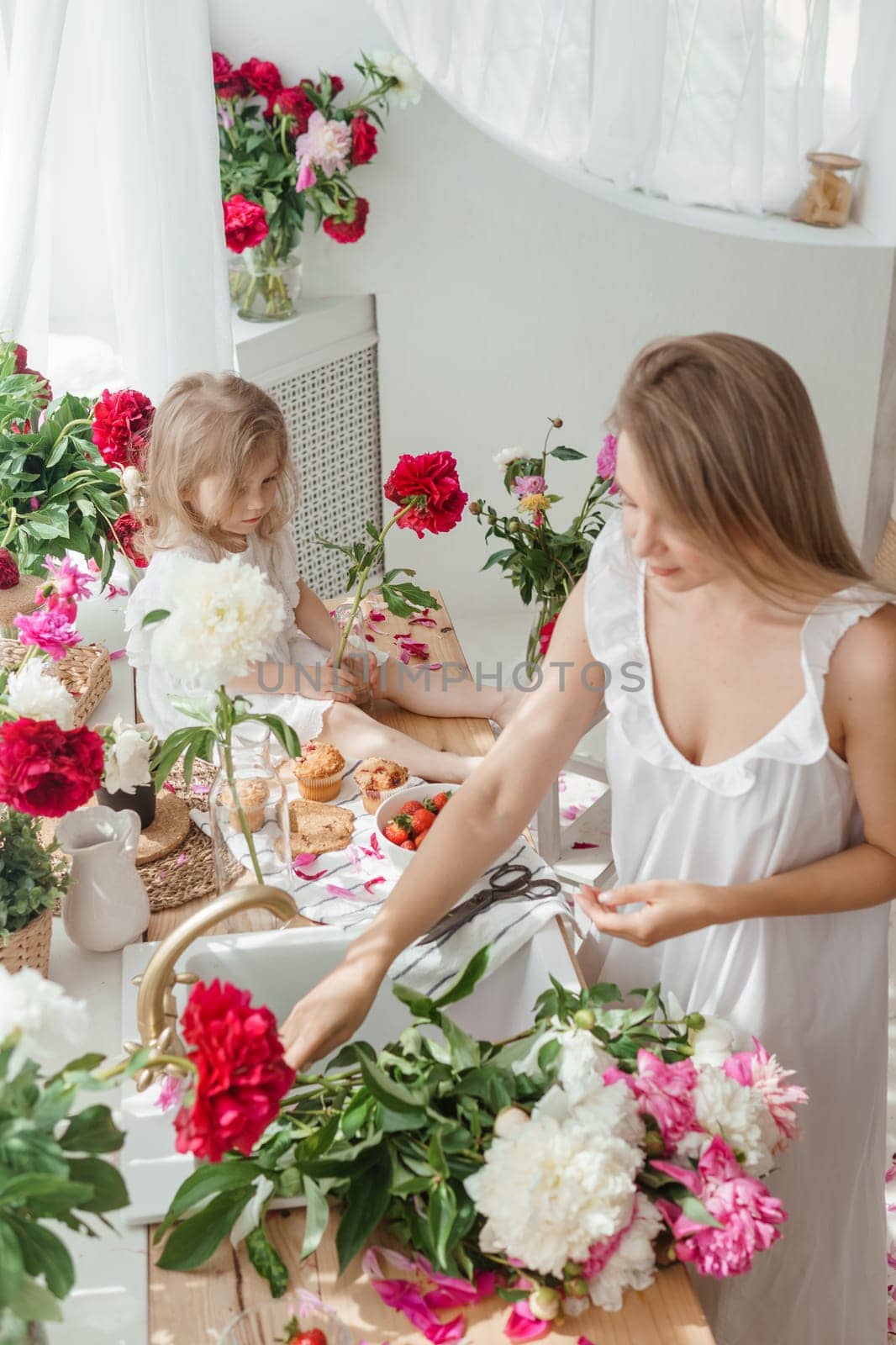 A little blonde girl with her mom on a kitchen countertop decorated with peonies. The concept of the relationship between mother and daughter. Spring atmosphere