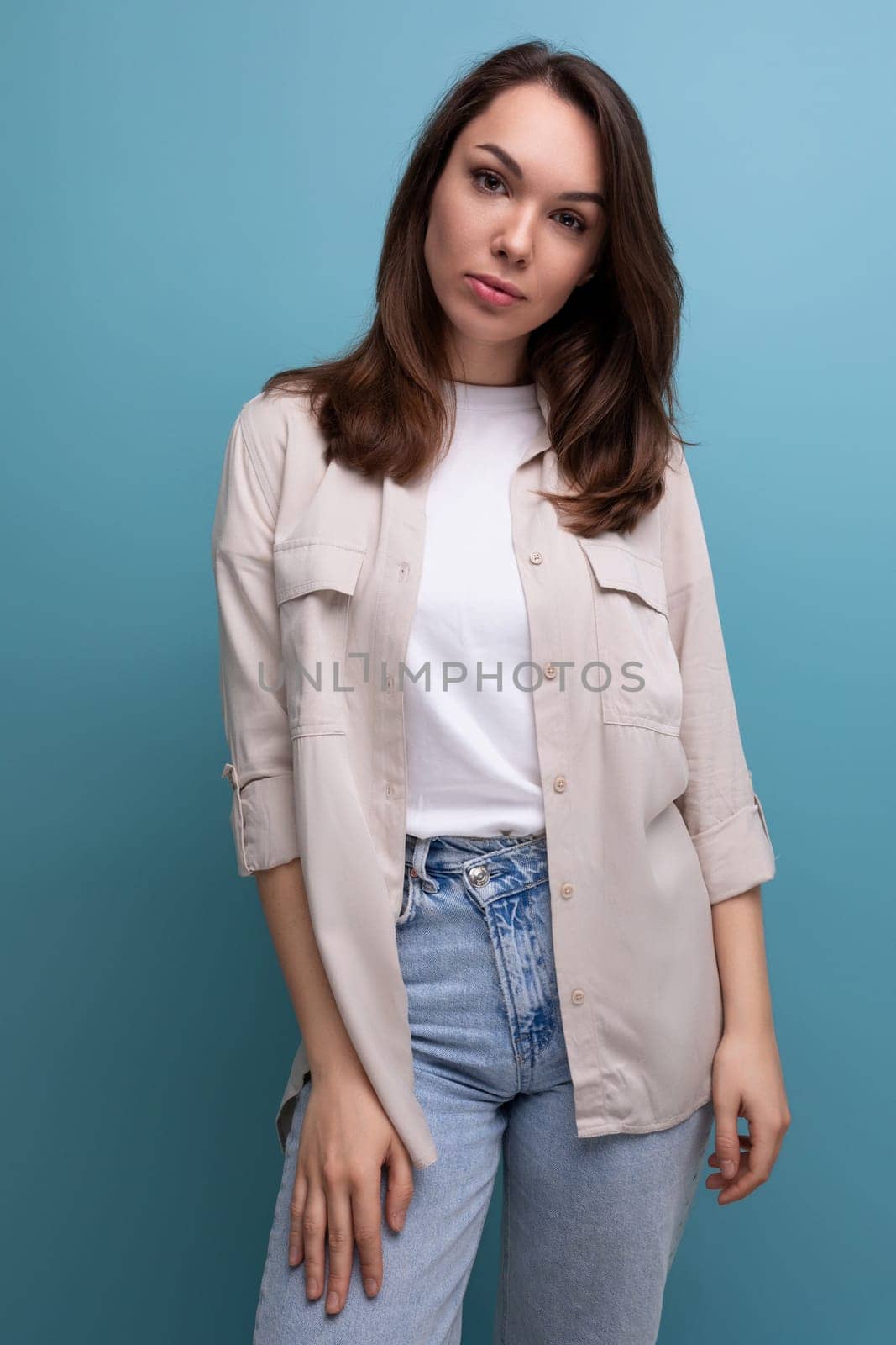 pretty 30s woman with chic well-groomed hair in a beige shirt on a blue background.