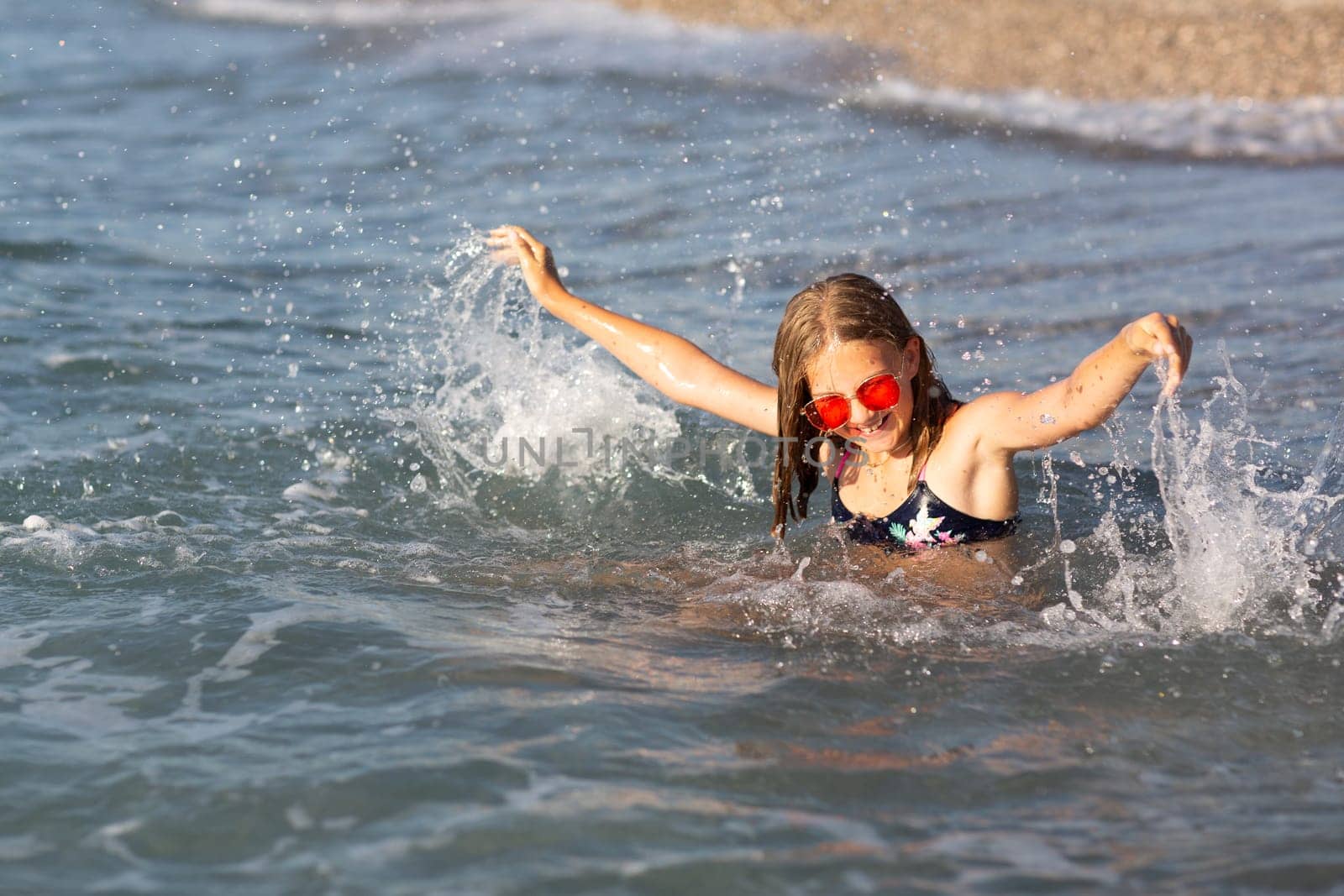 Teenage girl in pink sunglasses having fun on the beach in the sea, playing with splashes. Fun on summer hloiday concept. by Len44ik