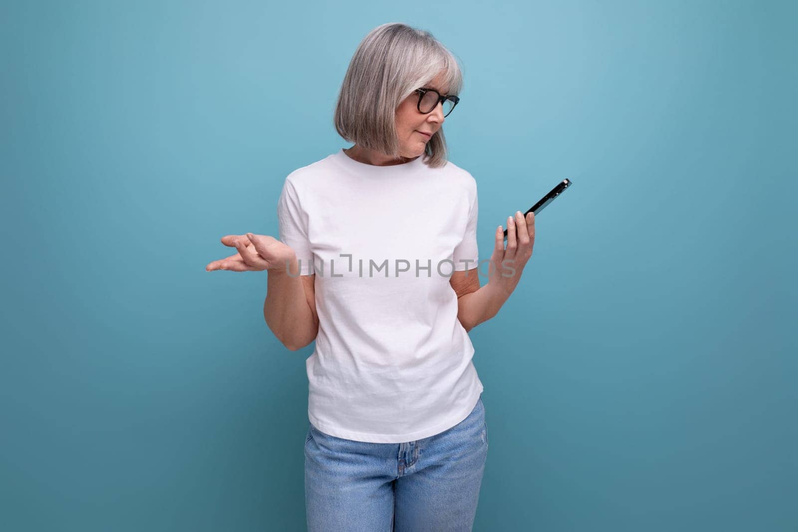 gray-haired mature woman studying digital technology smartphone on a bright studio background by TRMK