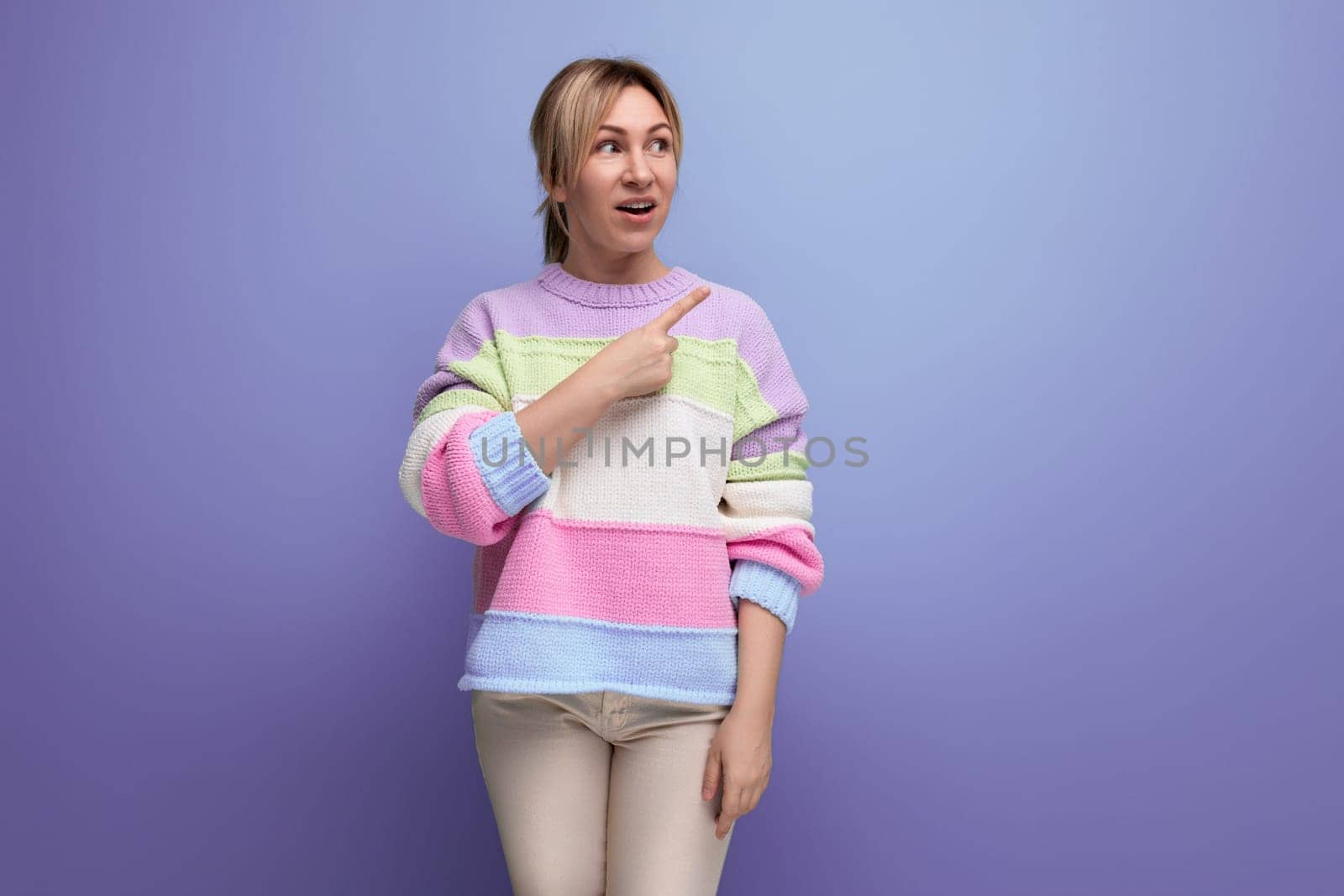 blond girl in surprise shows her hand to the side on a purple background with copy space by TRMK