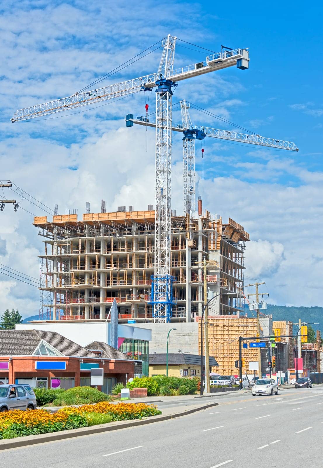 Construction of concrete high rise residential building with two cranes on blue sky background