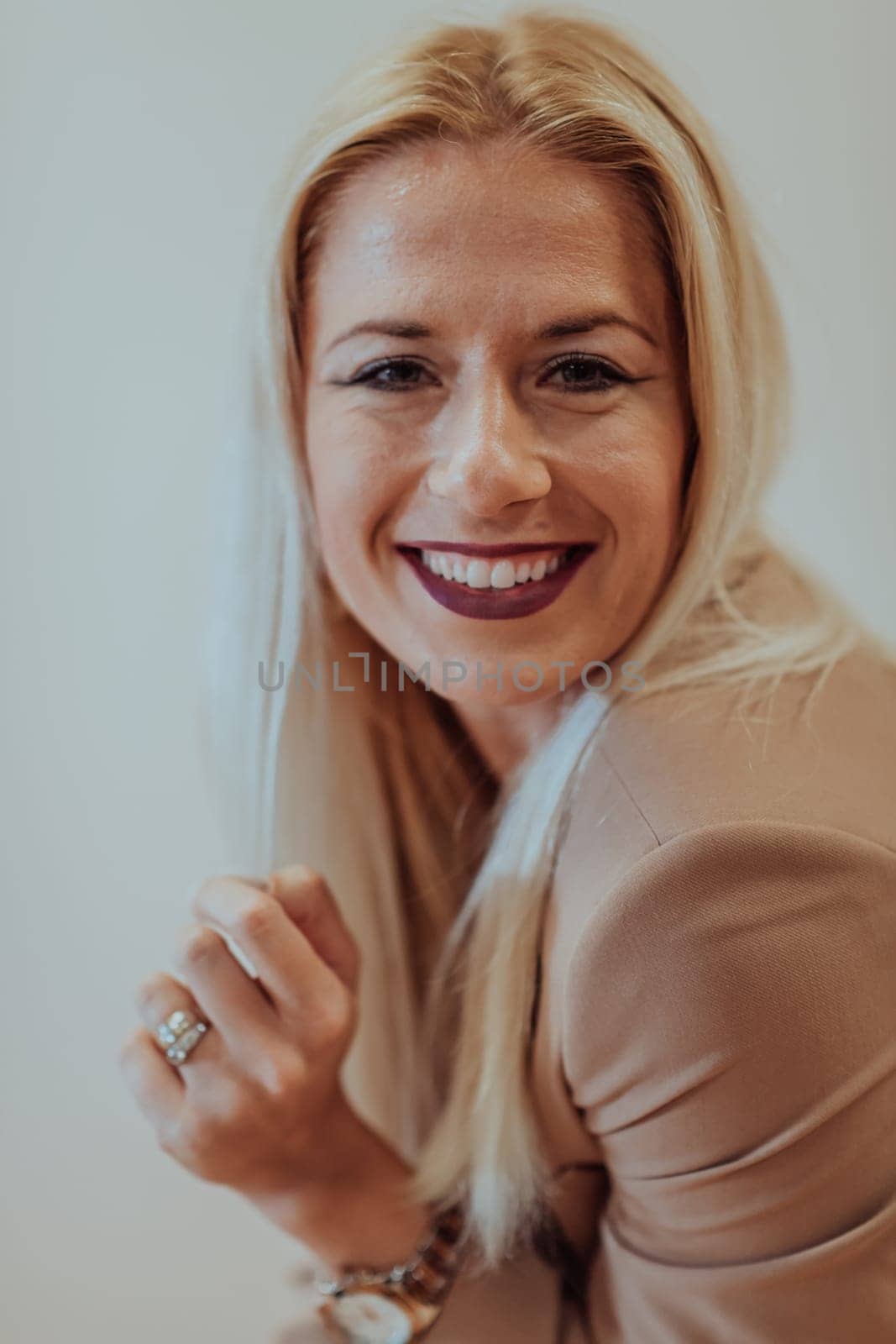 A confident and successful businesswoman, with a wide smile, strikes a pose in front of a beige background, exuding professionalism and elegance by dotshock