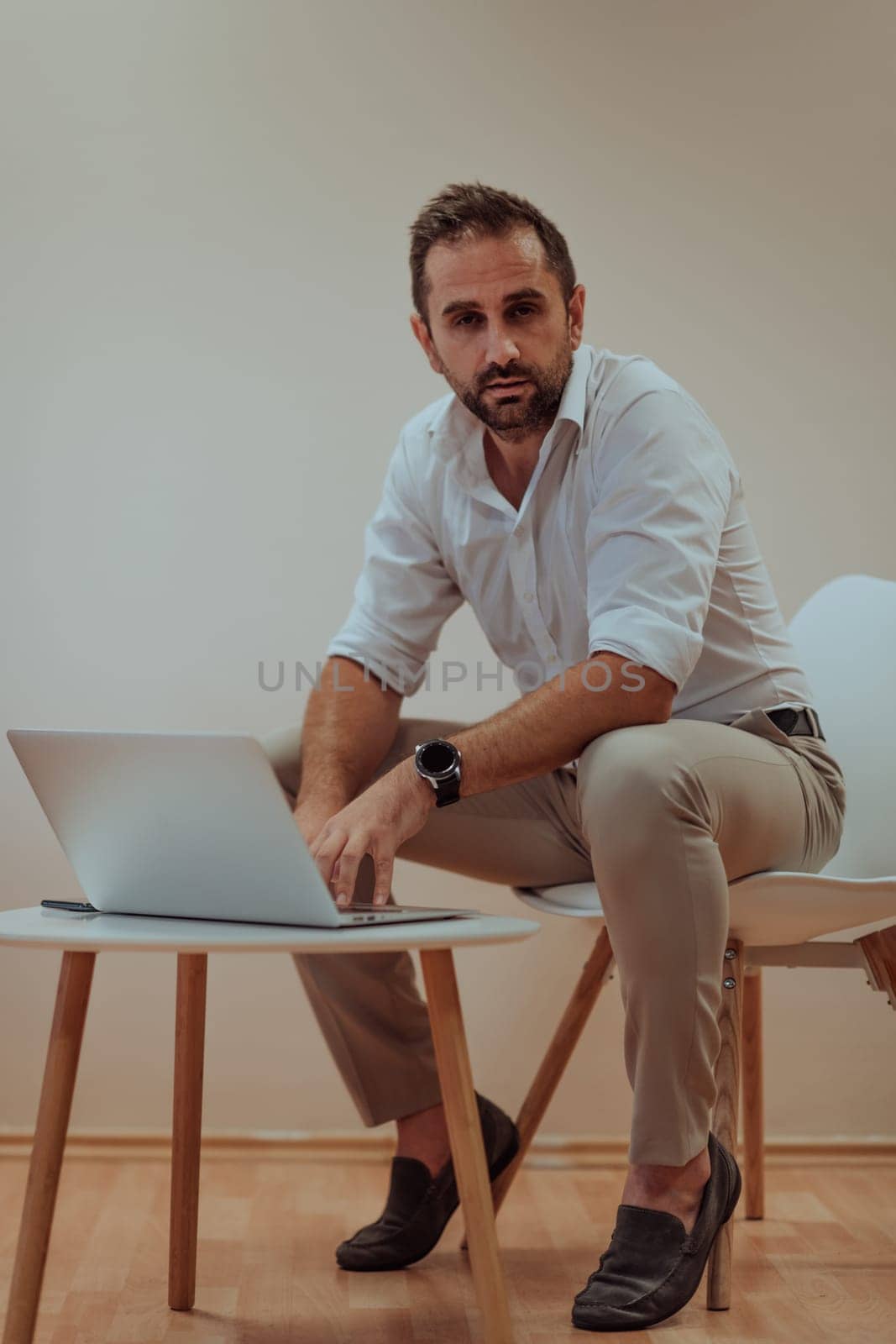 A confident businessman sitting and using laptop with a determined expression, while a beige background enhances the professional atmosphere, showcasing his productivity and expertise. by dotshock