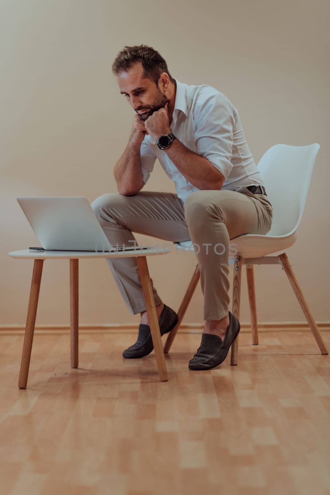 A confident businessman sitting and using laptop with a determined expression, while a beige background enhances the professional atmosphere, showcasing his productivity and expertise. by dotshock