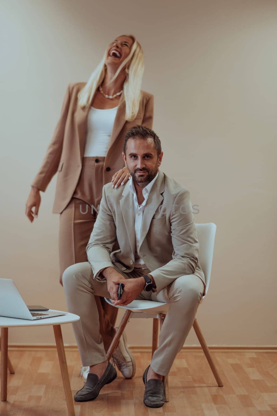 A business couple posing for a photograph together against a beige backdrop, capturing their professional partnership and creating a timeless image of unity and success. by dotshock