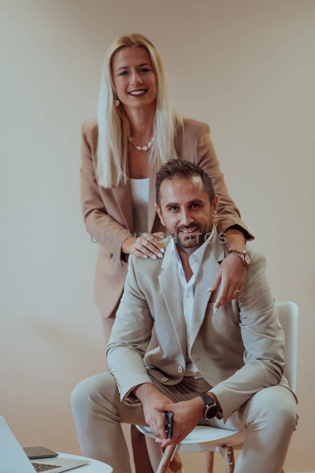 A business couple posing for a photograph together against a beige backdrop, capturing their professional partnership and creating a timeless image of unity and success. by dotshock