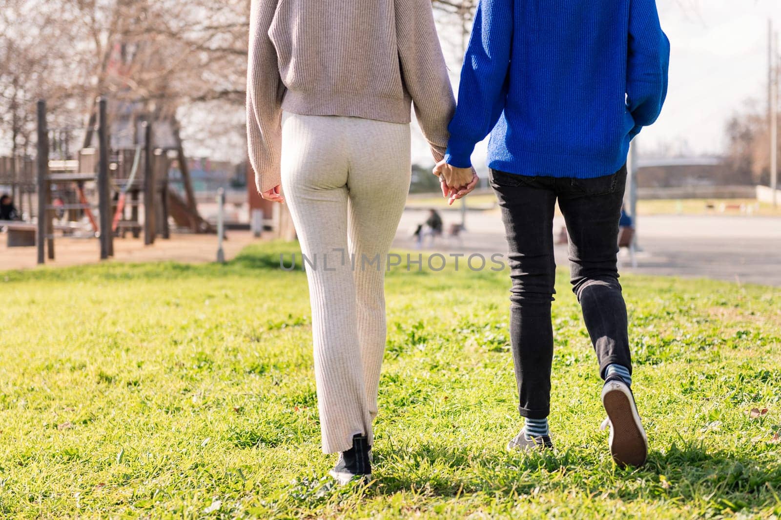 two unrecognizable women walking together holding hands in a city park, concept of freedom and love between people of the same sex