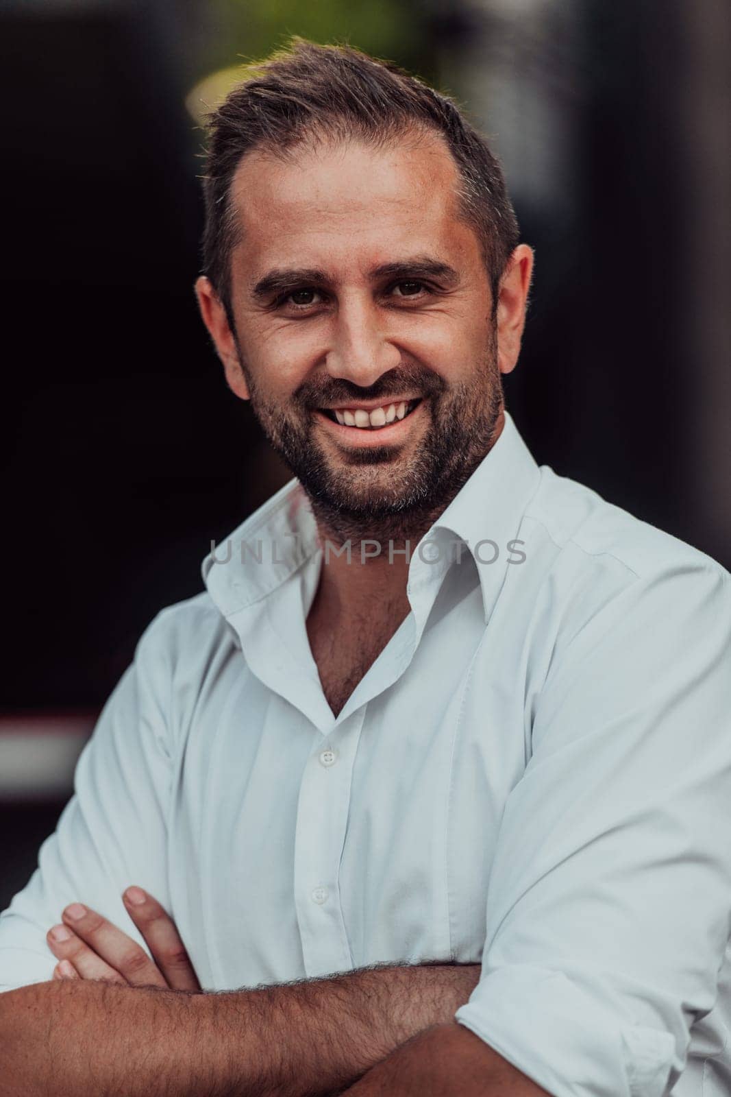 A successful businessman in a white shirt with crossed arms posing outdoors. High quality photo