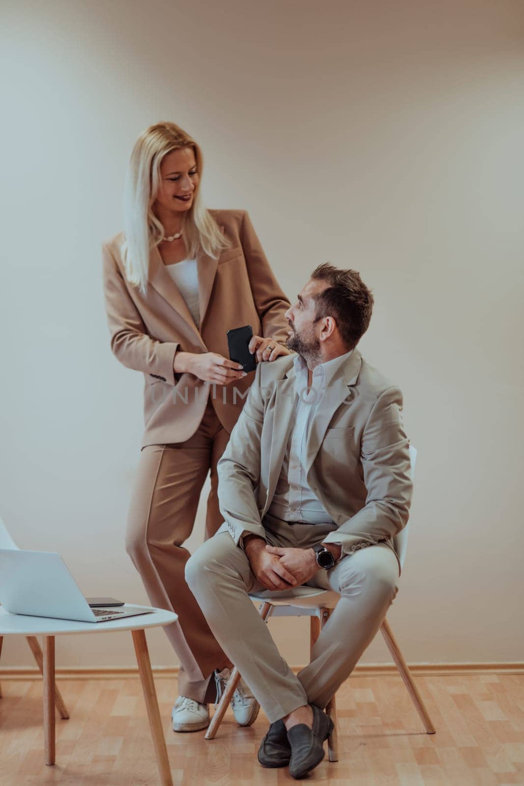 A business couple poses for a photograph together against a beige backdrop, capturing their professional partnership and creating a timeless image of unity and success