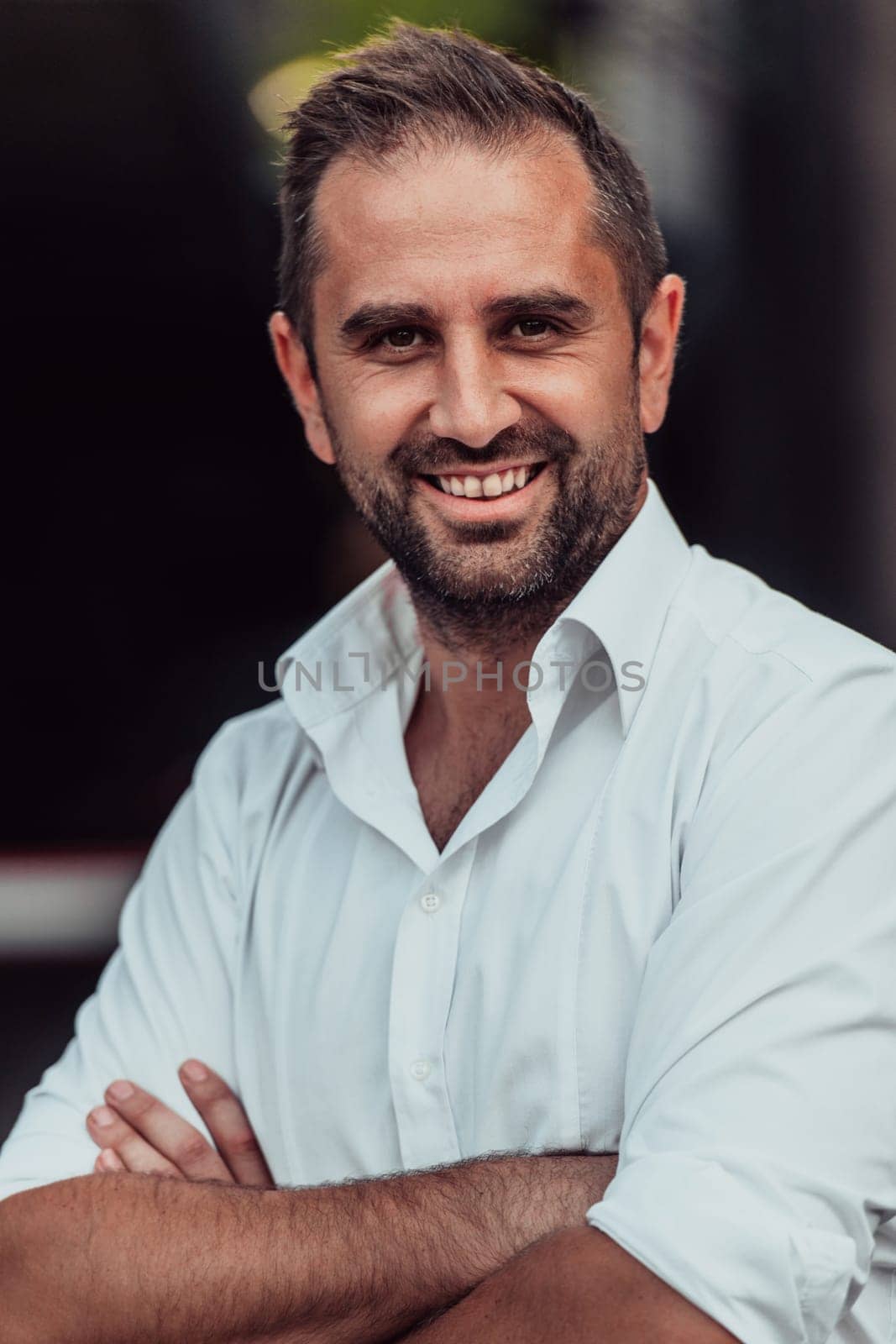 A successful businessman in a white shirt, with crossed arms, poses outdoors, confident expression on his face