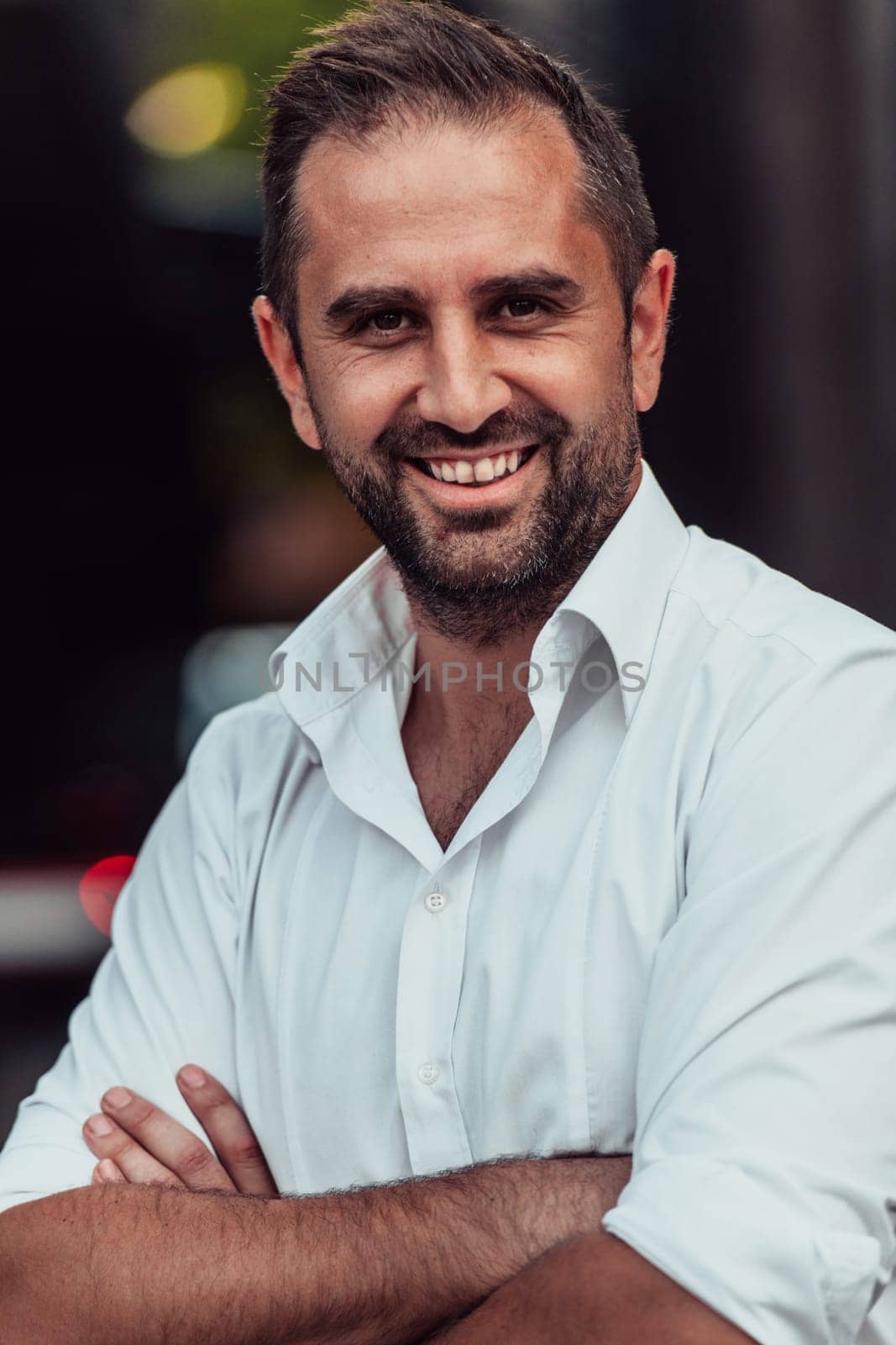 A successful businessman in a white shirt, with crossed arms, poses outdoors, confident expression on his face
