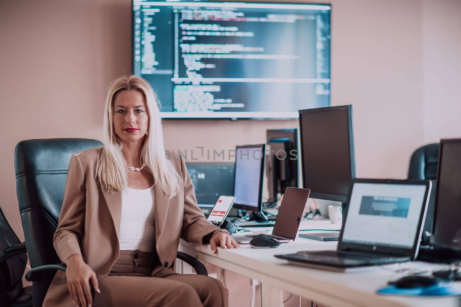 A businesswoman sitting in a programmer's office surrounded by computers, showing her expertise and dedication to technology