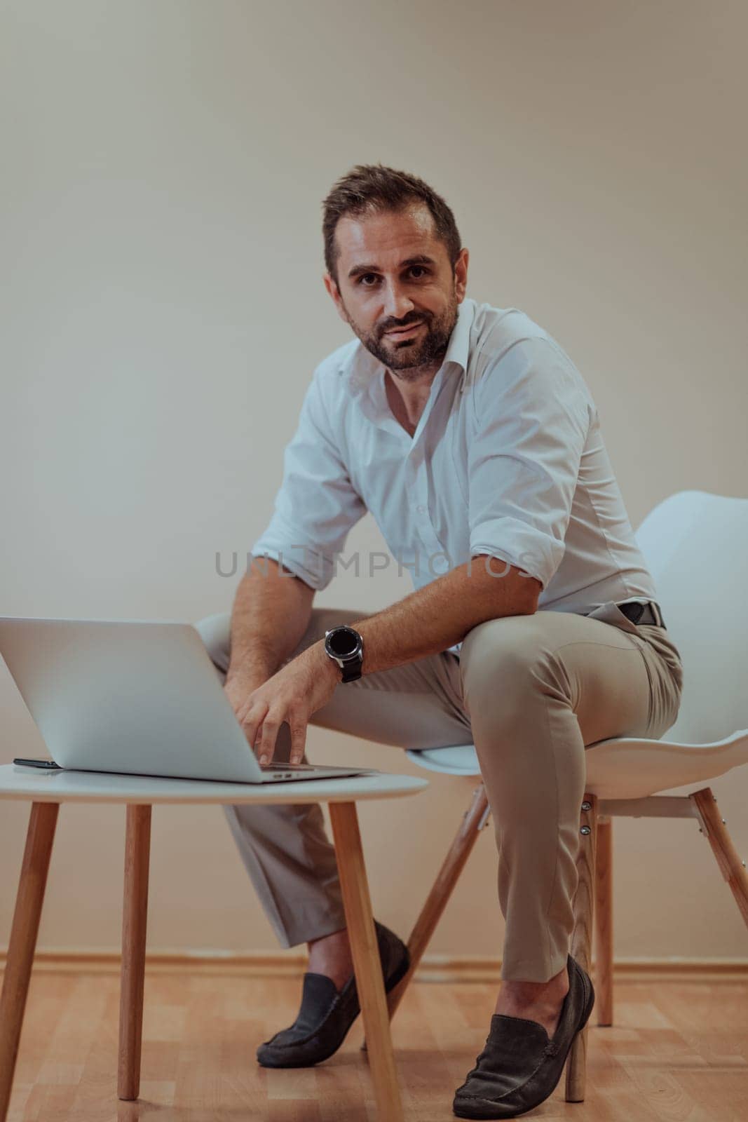 A confident businessman sitting and using laptop with a determined expression, while a beige background enhances the professional atmosphere, showcasing his productivity and expertise. by dotshock