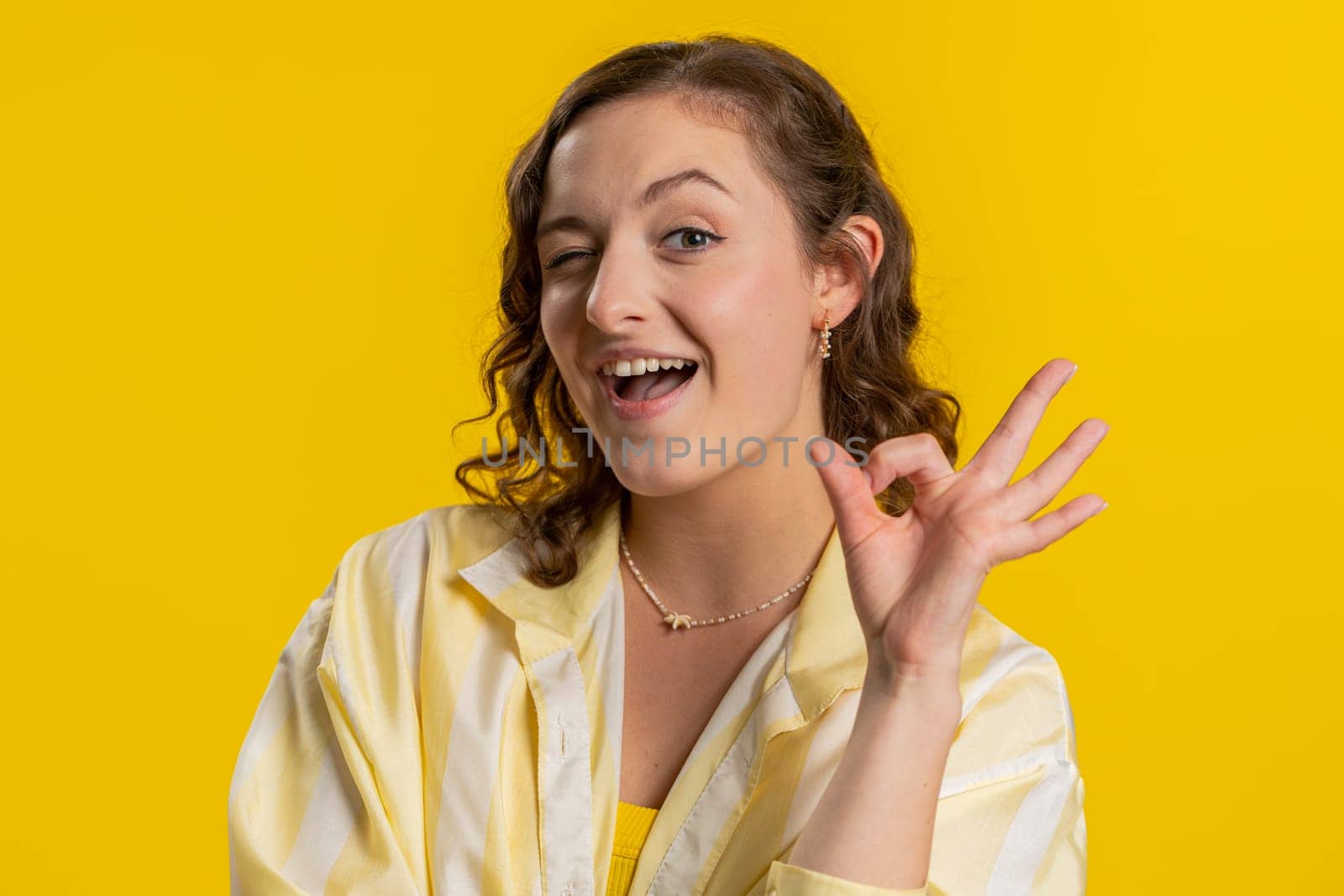 Okay. Joyful happy young woman looking approvingly at camera showing approve feedback gesture like Ok sign positive something good. Pretty girl isolated on yellow background. People sincere emotion
