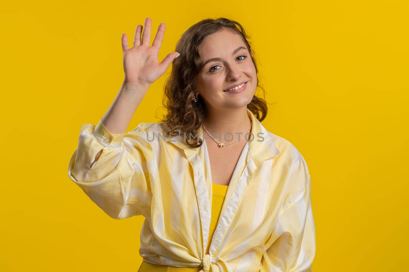 Come here, join us. Welcome. Brunette attractive woman showing inviting gesture with hands, ask to join, beckoning to coming, gesturing hello, goodbye. Pretty girl isolated on yellow studio background