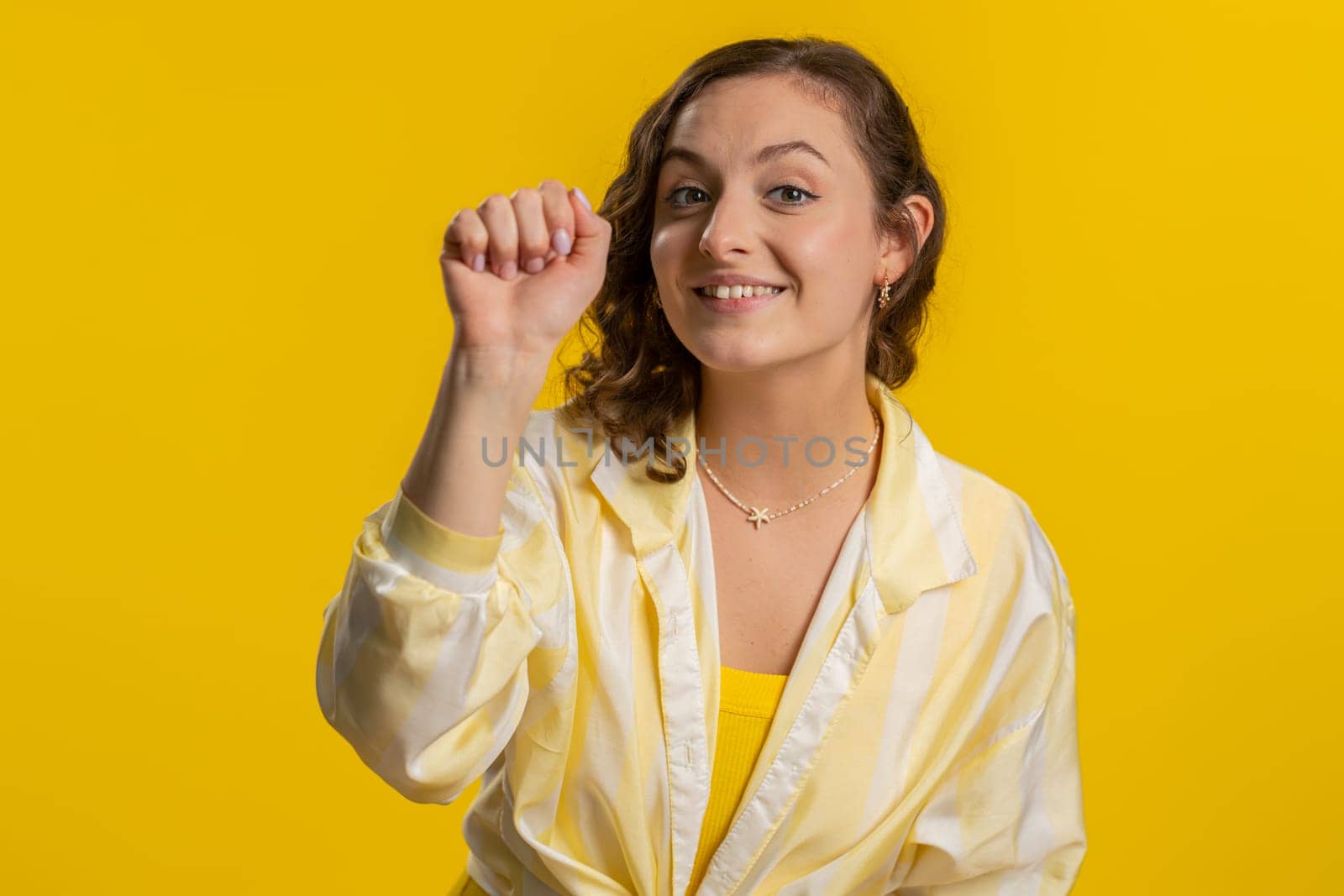 Knock-knock who is there. Excited young woman knocking door gesture asking who is at home, feeling embarrassed, no idea, being clueless and uncertain. Girl isolated alone on studio yellow background