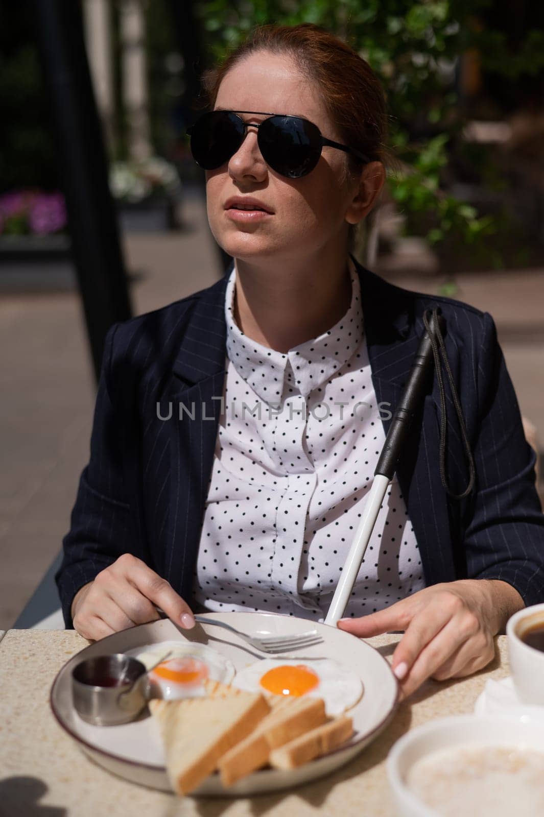 A blind woman in a business suit eats scrambled eggs in a street cafe