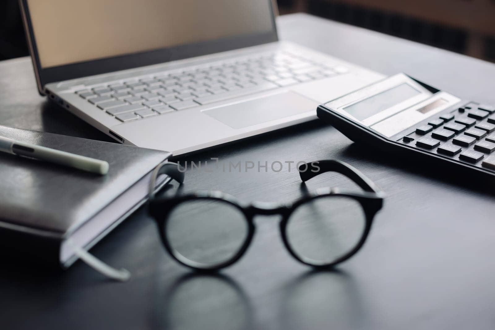 Finance Professional's Workspace: Office Desk with Laptop, Calculator, and Glasses - Exploring Accountancy, Tax Planning, Savings, and Modern Business Concepts.