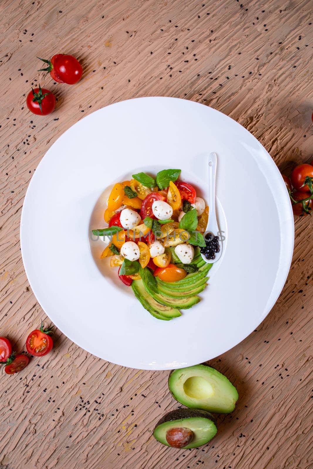 top view salad with avacado, mozzarella and tomatoes in a white plate by Pukhovskiy