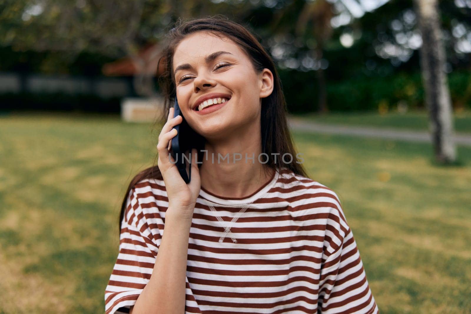 caucasian woman smiling smartphone park healthy lifestyle using palm mobile happy beautiful summer grass phone jeans shirt application nature blogger person tree