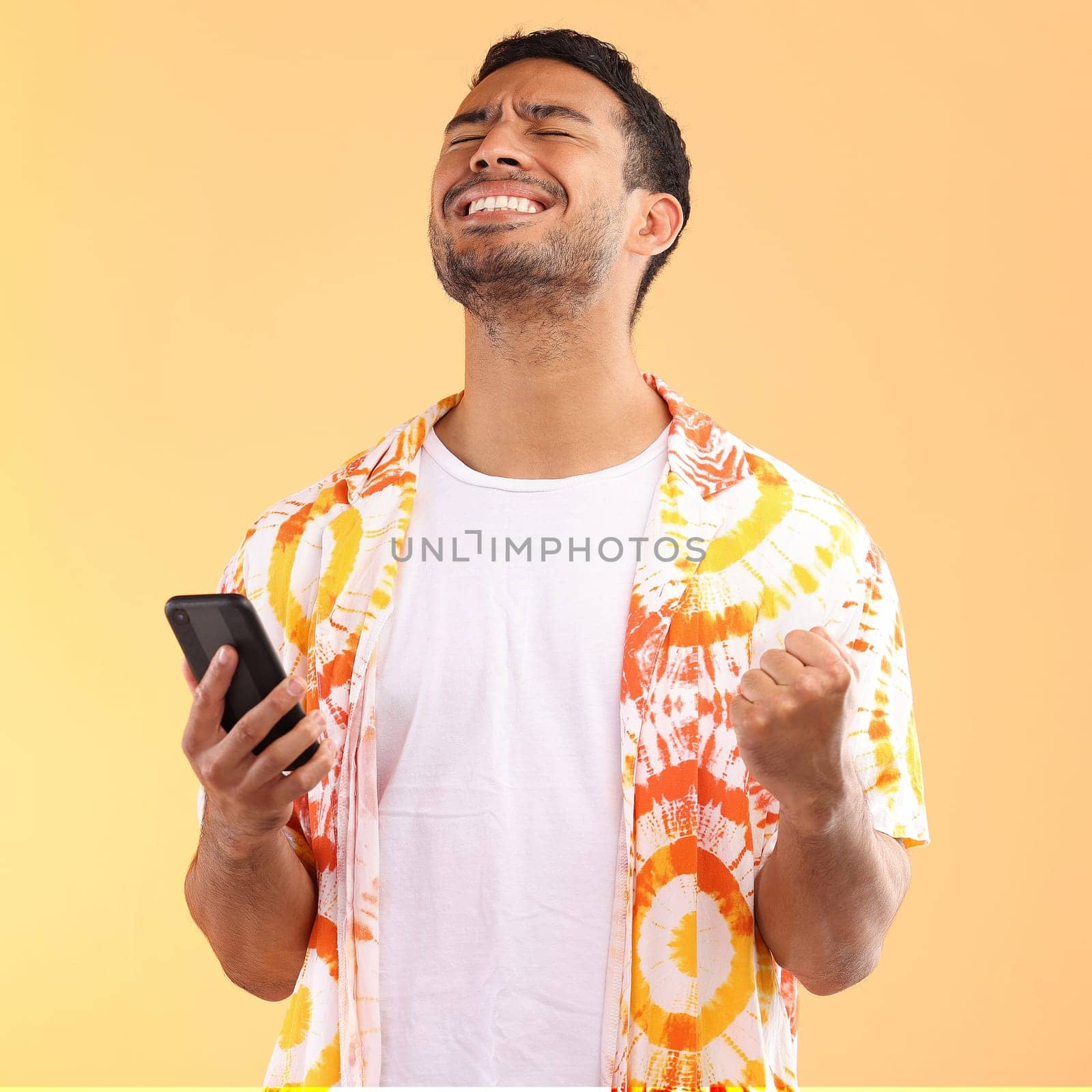 Winner, celebration and man with phone in studio isolated on yellow background. Winning, cellphone or happy male model holding mobile smartphone while celebrating goals achievement, target or success.