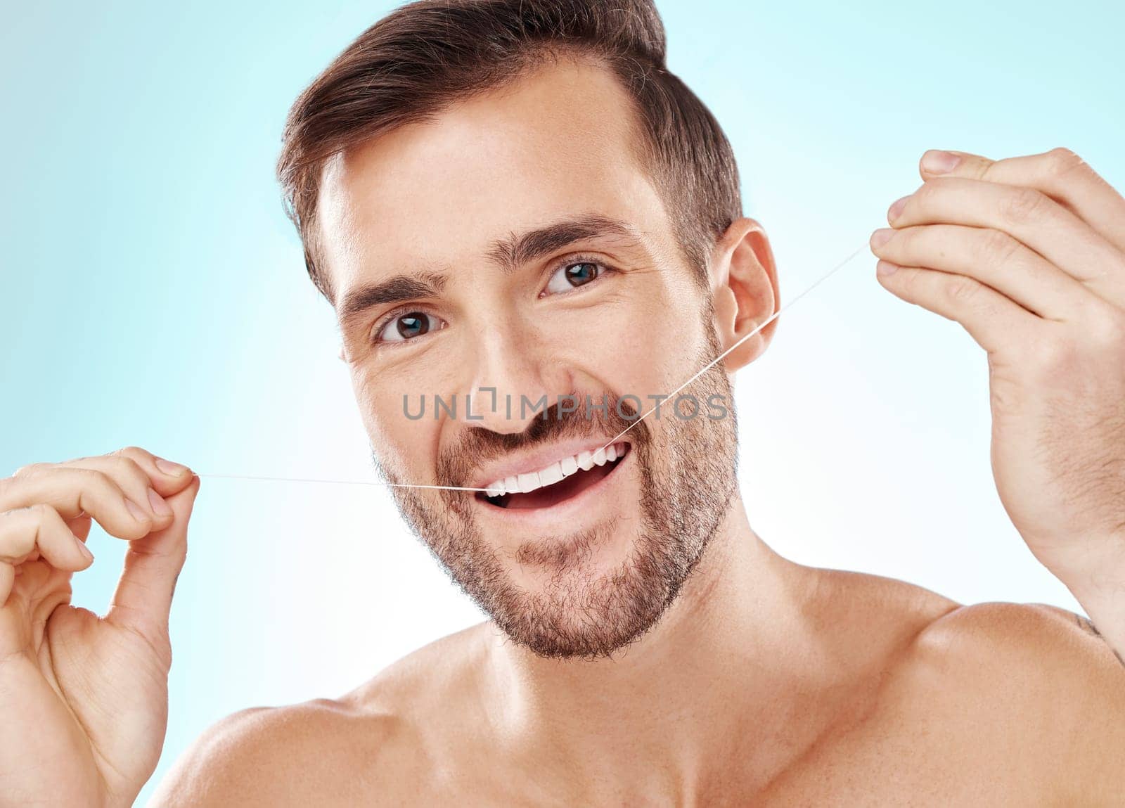 Face, portrait and man with dental floss in studio isolated on a blue background. Oral health, hygiene or happy male model flossing teeth for wellness, cleaning or fresh breath, cosmetics or gum care.