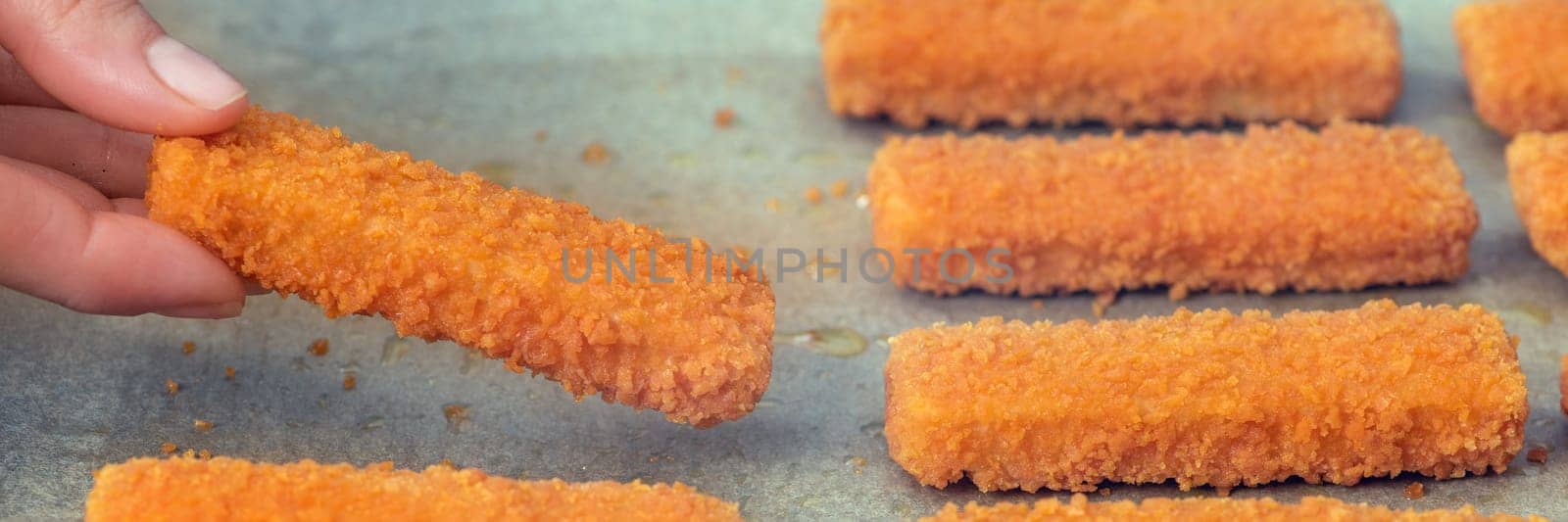 The hand lays out the fish fingers on the frying paper. The concept of frying fish sticks in the oven. Side view. Close-up. High quality photo