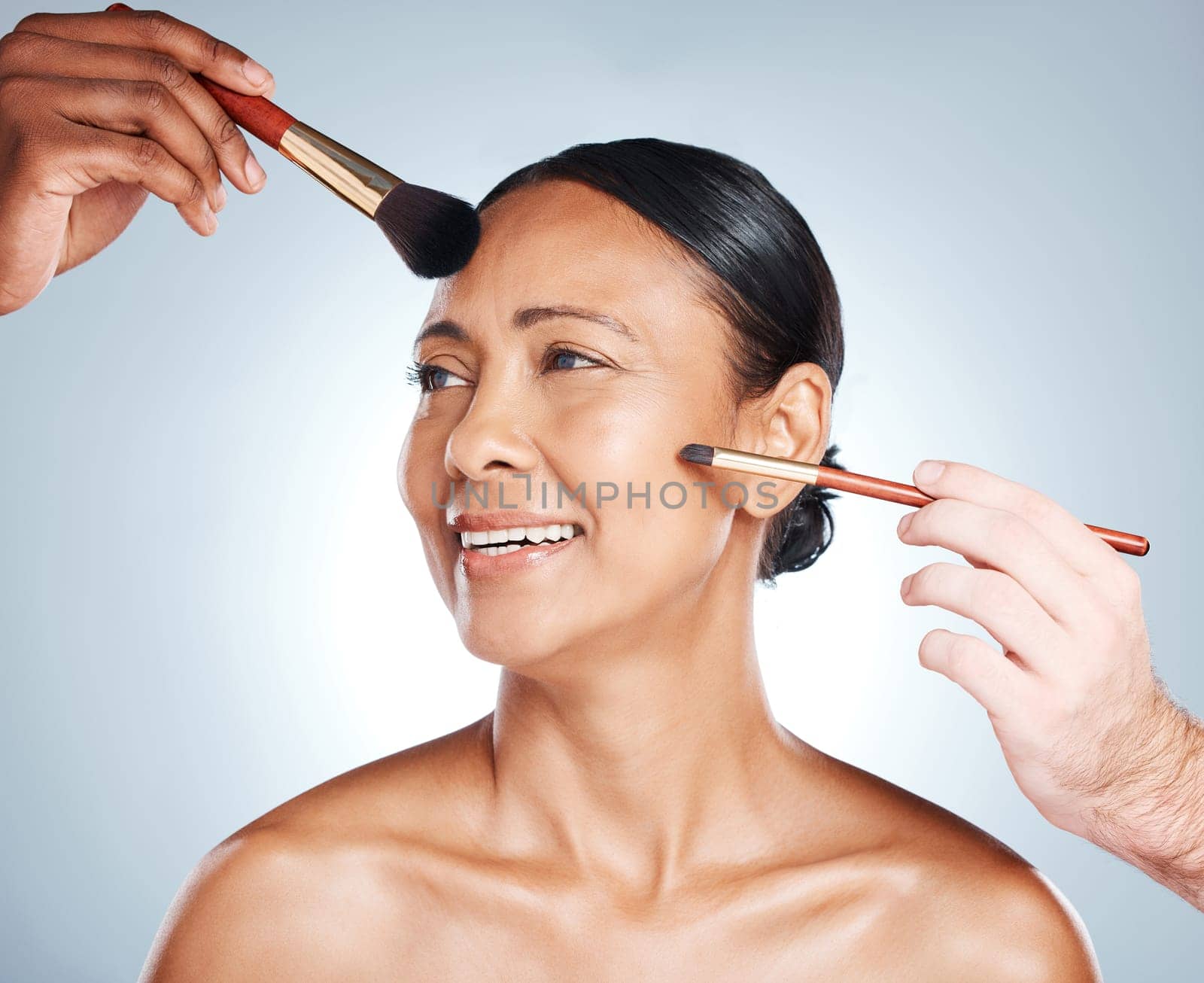 Woman, hands and smile for beauty makeup, cosmetics or facial treatment against a grey studio background. Happy female model smiling in satisfaction for skincare, pamper and brushes on her face.