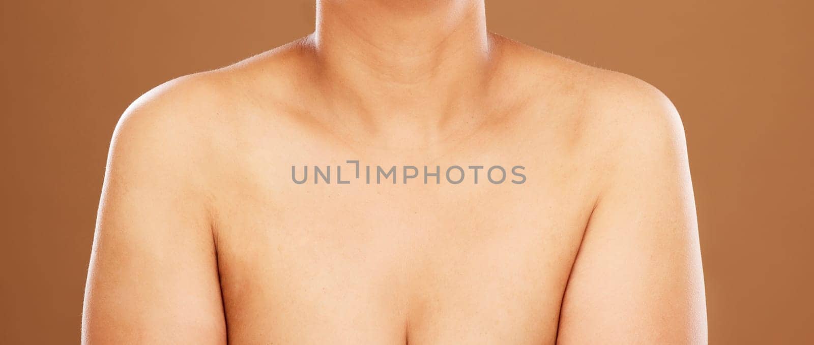 Woman, chest and skincare on a brown studio background for health, wellness and breast cancer awareness. Human body, skin and bust of a female model posing naked for healthcare and self care by YuriArcurs