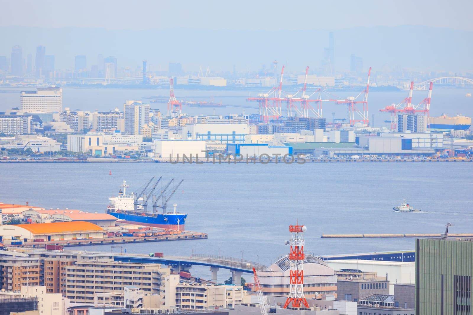 Cargo ship docked at Kobe port with loading cranes and city skyline in distance. High quality photo