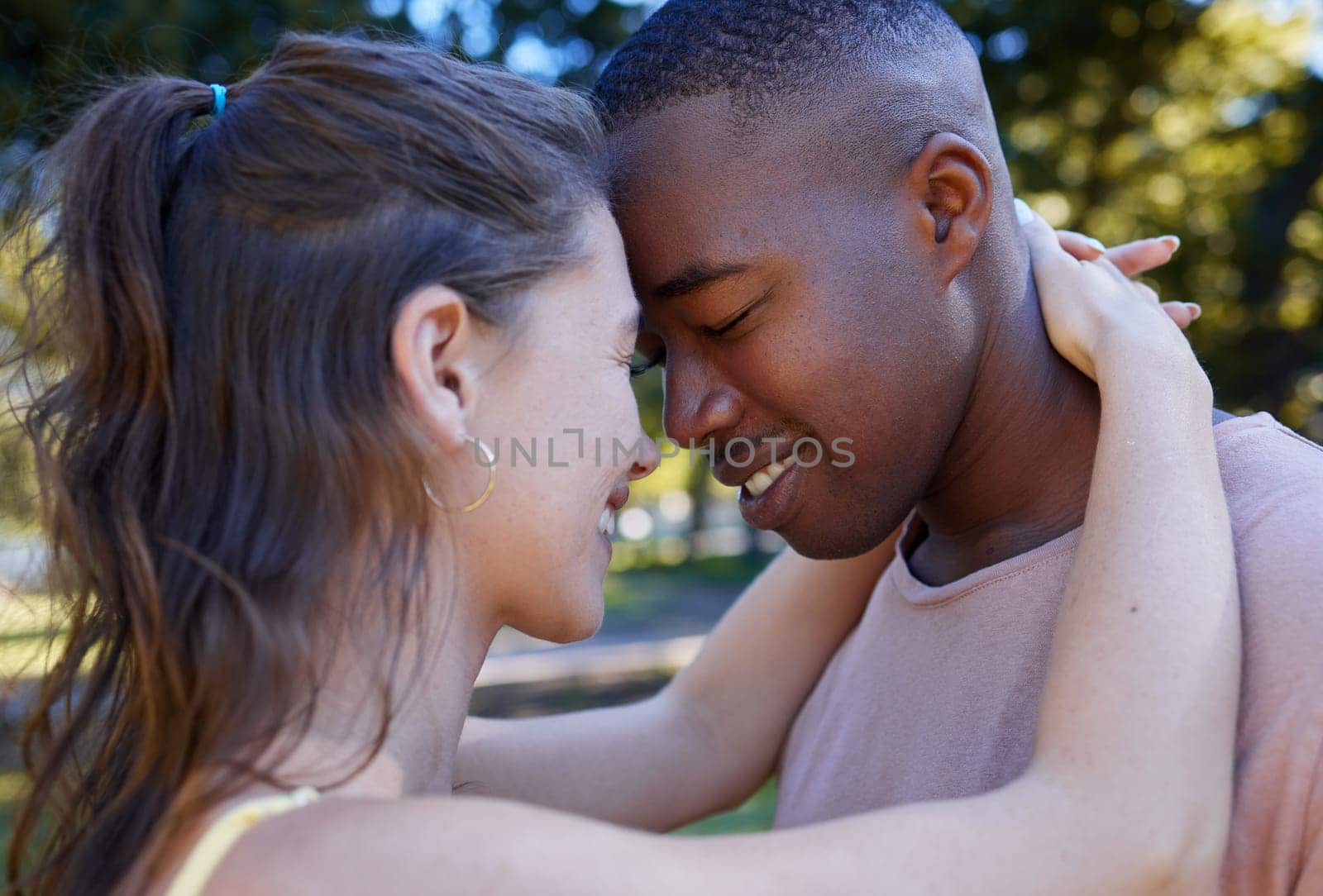 Love, park and face with an interracial couple bonding or hugging outdoor together on a romantic date in nature. Summer, romance and diversity with a man and woman dating outside in a green garden by YuriArcurs