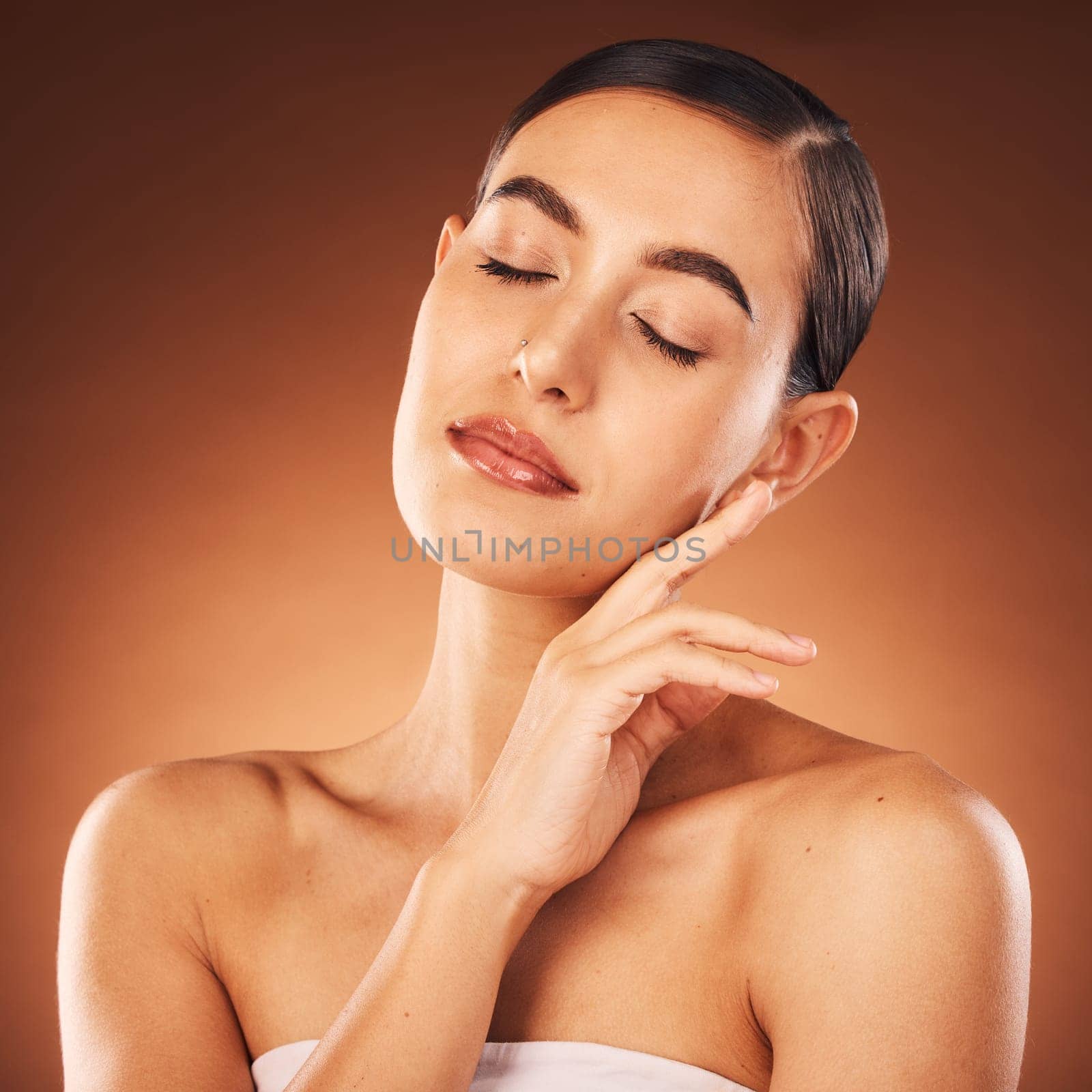 Face, beauty and skincare with a model woman in studio on a brown background for wellness or luxury. Spa, facial and cosmetics with an attractive young female posing to promote a skin product.