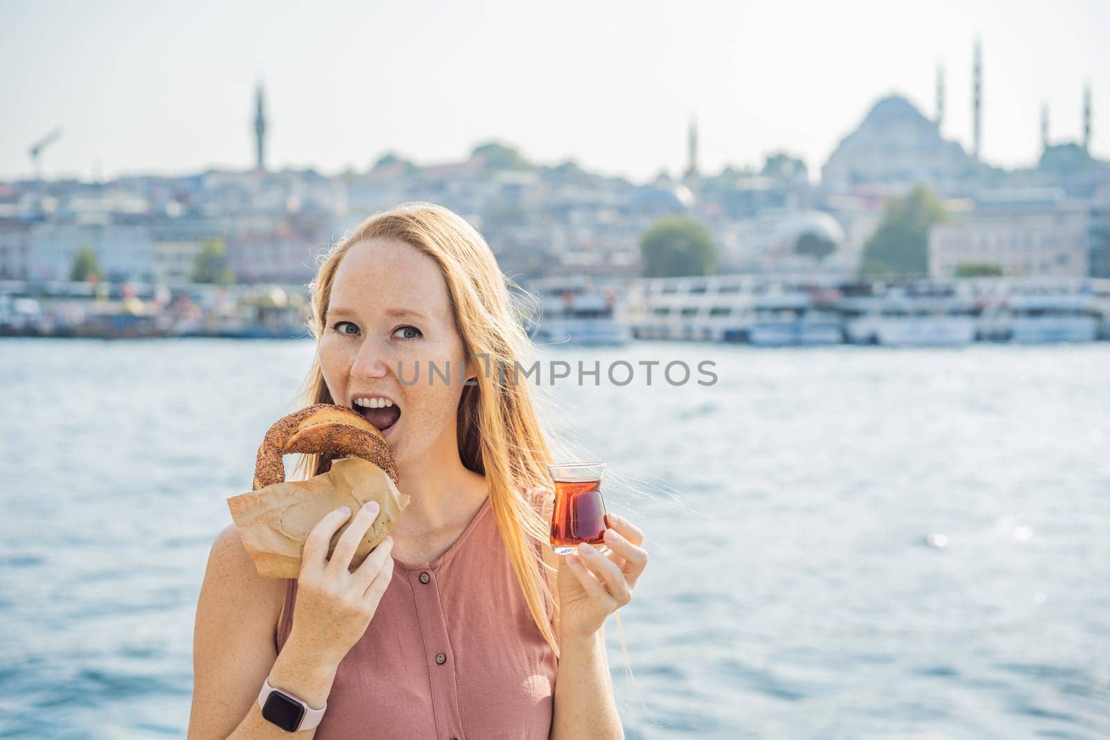 Woman in Istanbul having breakfast with Simit and a glass of Turkish tea. Glass of Turkish tea and bagel Simit against golden horn bay in Istanbul, Turkey. Turkiye.