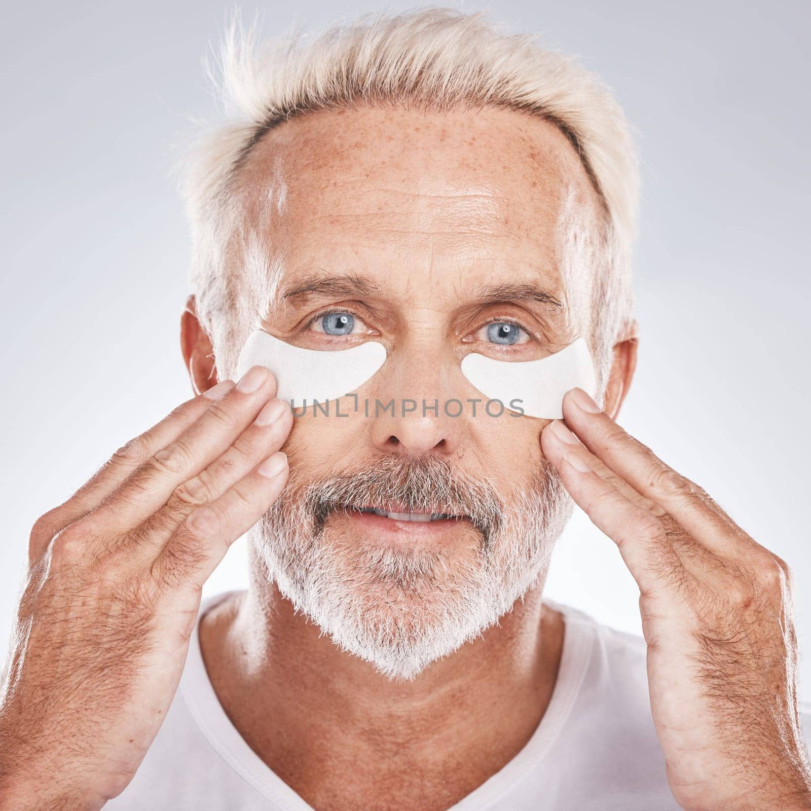 Senior man with collagen eyes mask in skincare, dermatology facial and face cosmetics advertising in studio portrait. Elderly model with hands application of eye patch, anti aging product and beauty by YuriArcurs