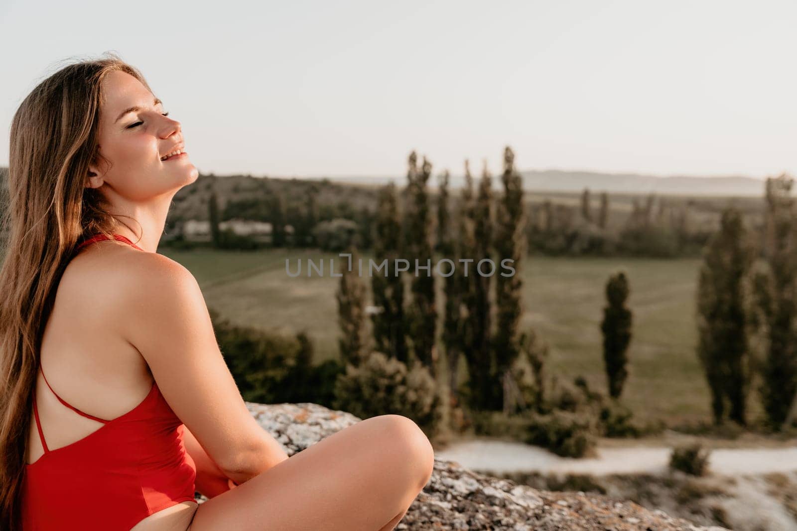 Well looking middle aged woman with long hair, fitness instructor in leggings and tops doing stretching and pilates on the rock near forest. Female fitness yoga routine concept. Healthy lifestyle by panophotograph