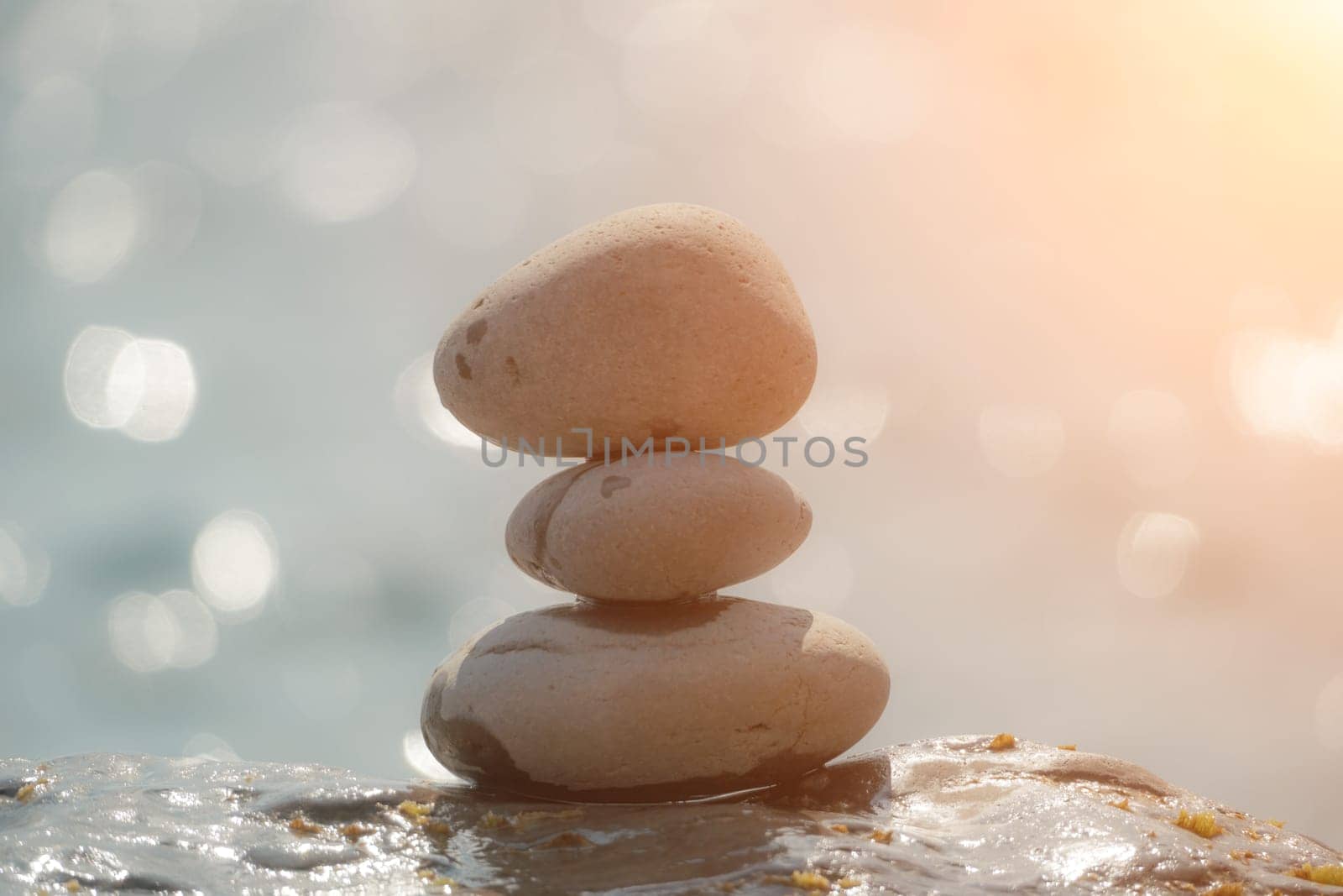 Balanced rock pyramid on sea pebbles beach, sunny day and clear sky at sunset. Golden sea bokeh on background. Selective focus, zen stones on sea beach, meditation, spa, harmony, calm, balance concept by panophotograph