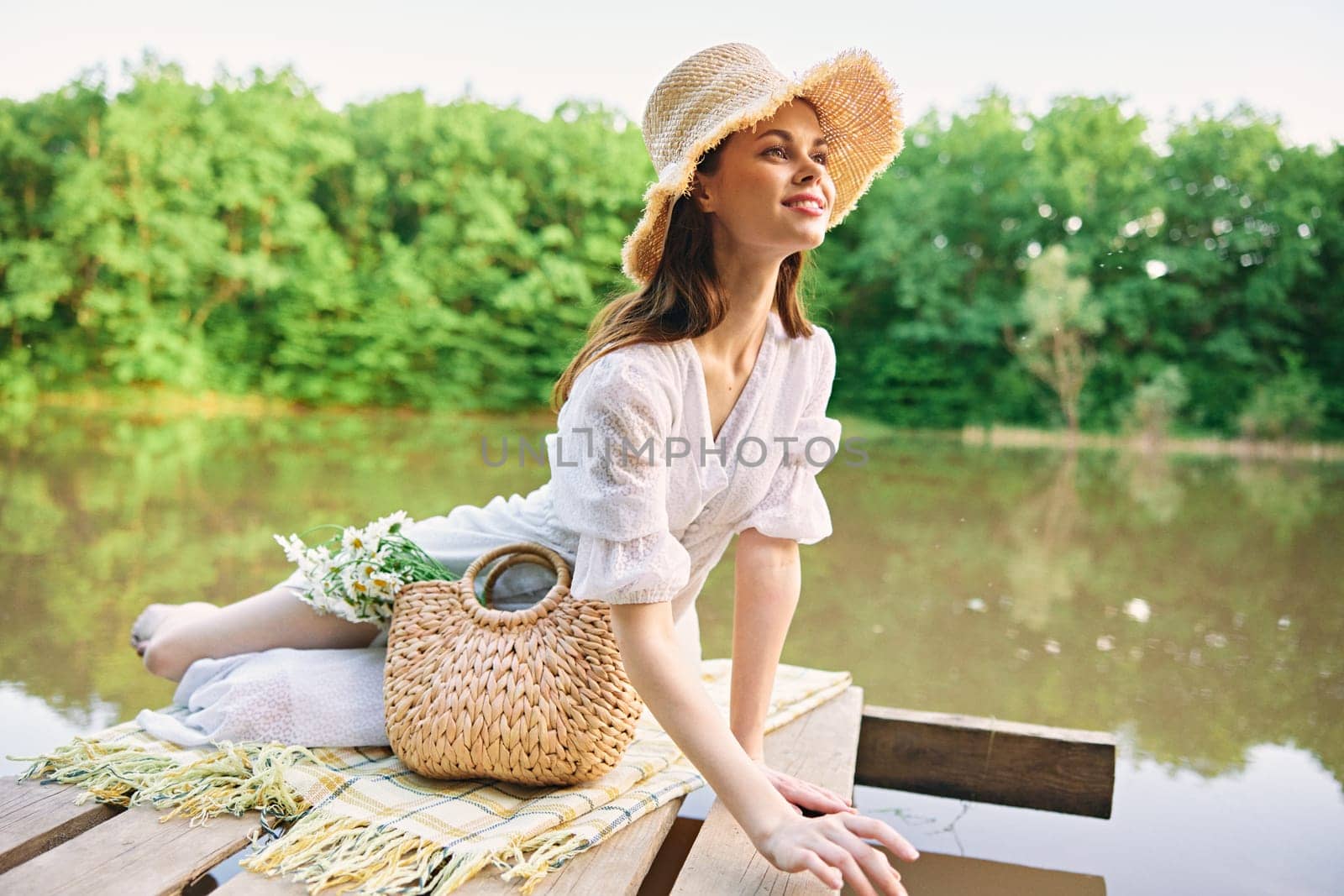 happy woman in a wicker hat resting in nature by the lake in summer by Vichizh