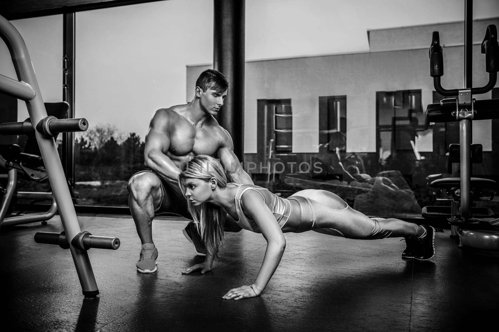 Sportive woman doing plank exercise training back and press muscles with trainer. Sport fitness workout strength power concept. Work in the gym. Black and white