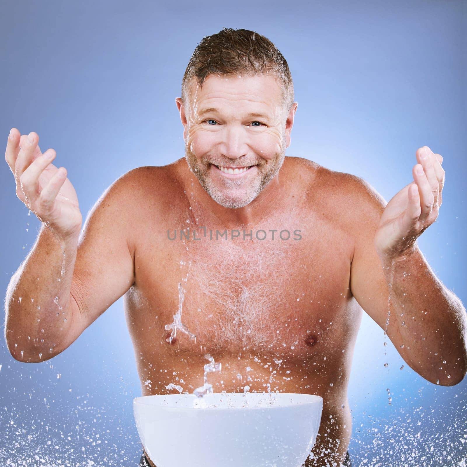 Skincare, water and man washing face in a studio for a beauty, natural and cosmetic routine. Happy, smile and portrait of a senior male model doing a facial cleansing treatment by a purple background.